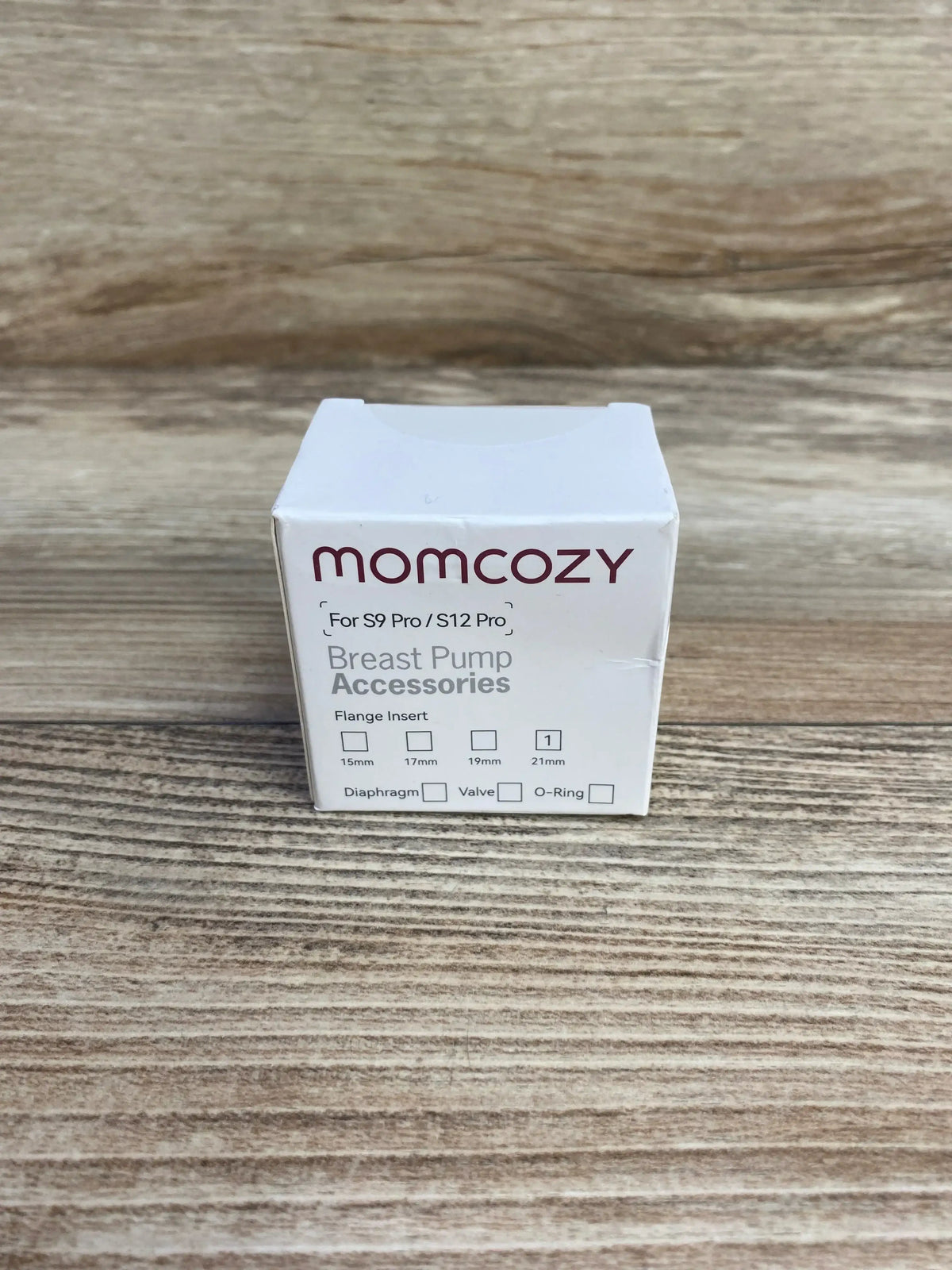 Front view of NEW Momcozy breast pump accessories box for S9 Pro and S12 Pro with 21mm flange insert diaphragm and valve marked on wood plank floor
