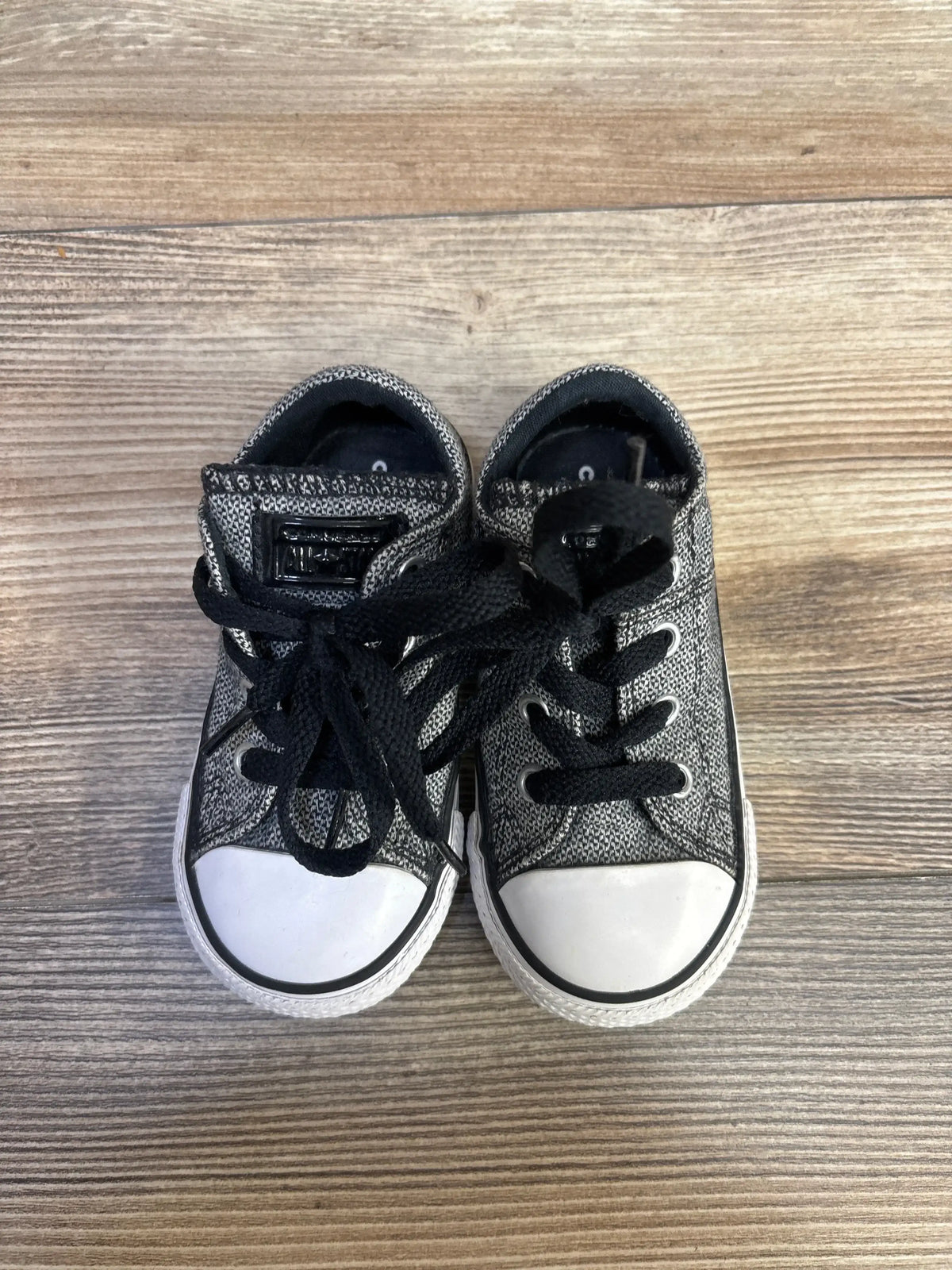 Top view of Converse Madison Ox low-top toddler sneakers in grey showing white rubber toe caps and black laces on wood floor