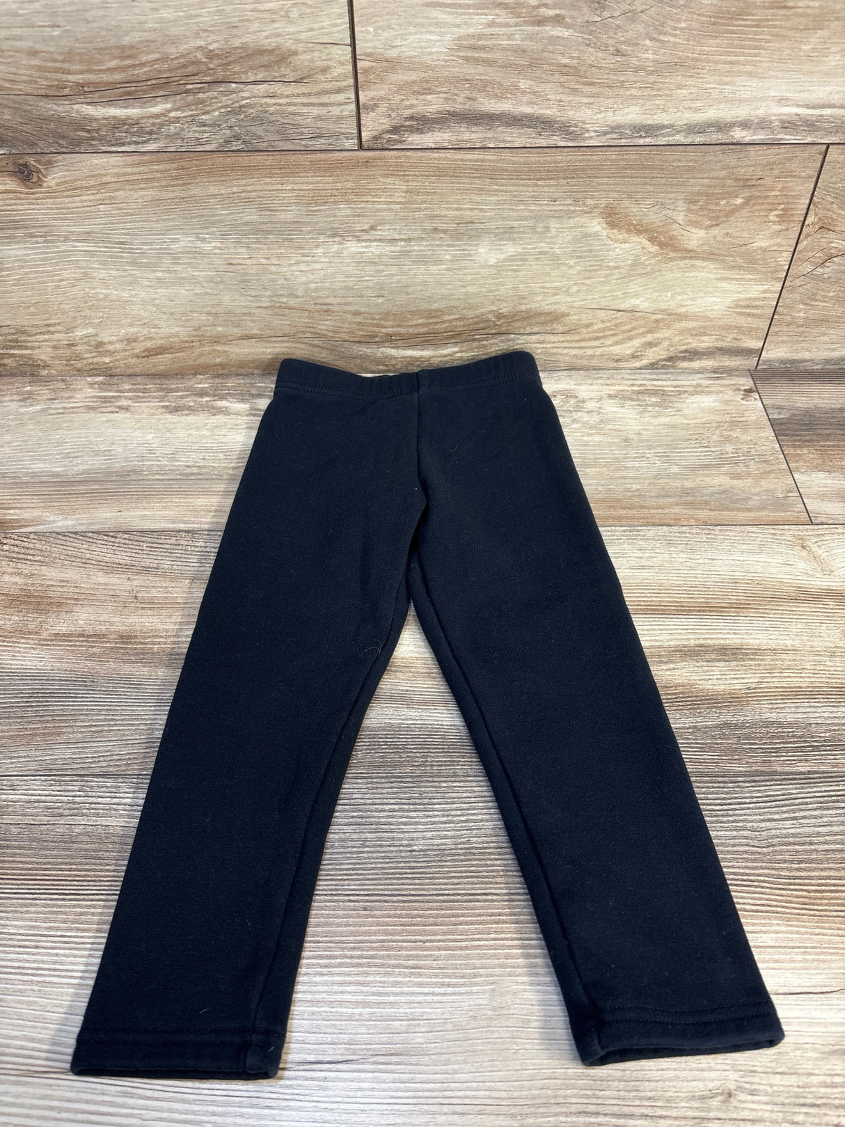 Black toddler leggings displayed on wood floor, kids clothing resale