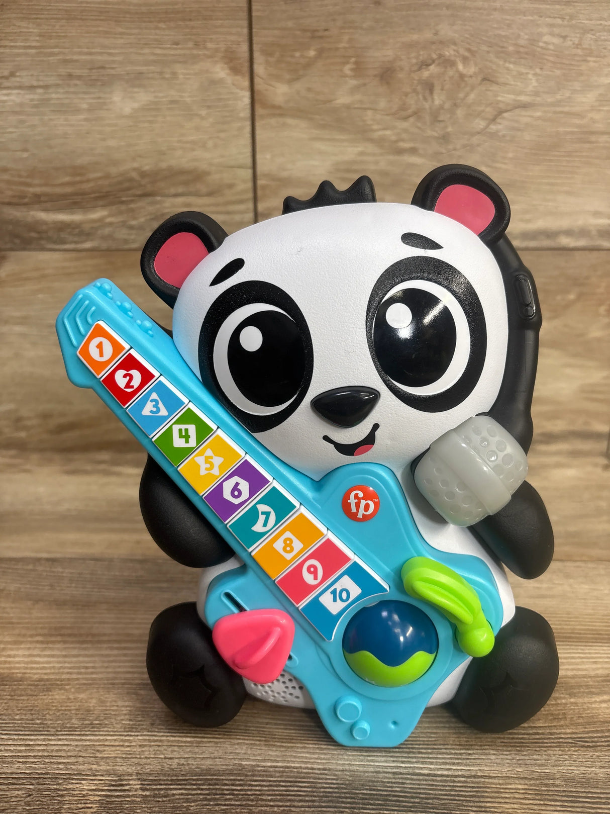 Colorful panda-shaped toddler toy holding a blue plastic guitar with numbered keys on wood background
