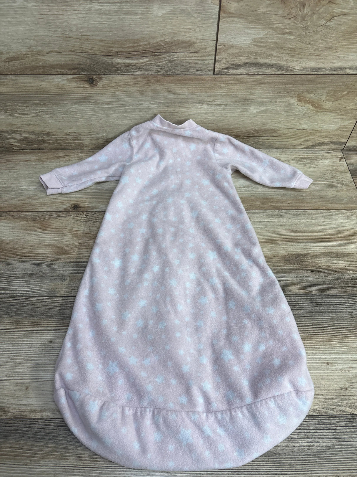 Pink baby sleeper gown with white star pattern on wooden floor