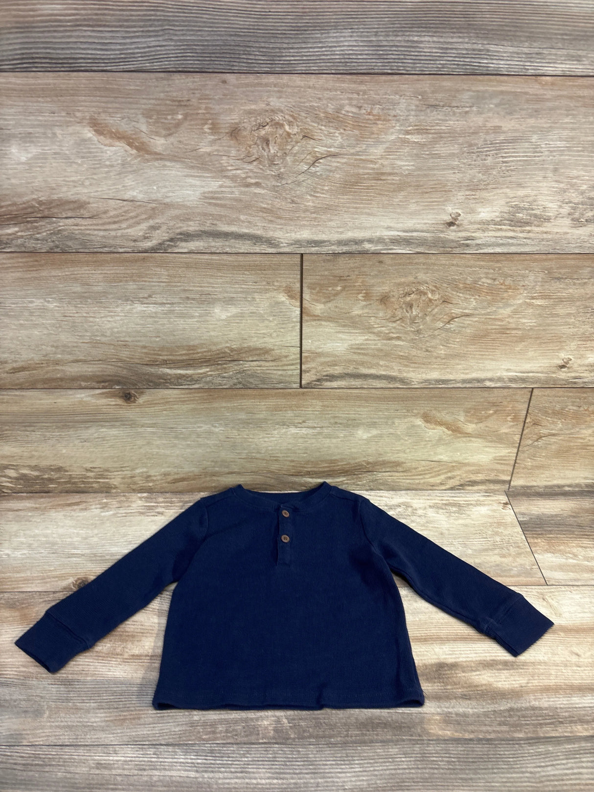 Flat lay of Children’s Place navy thermal henley shirt (18–24 months) showing long sleeves, two-button placket and waffle texture on wood background