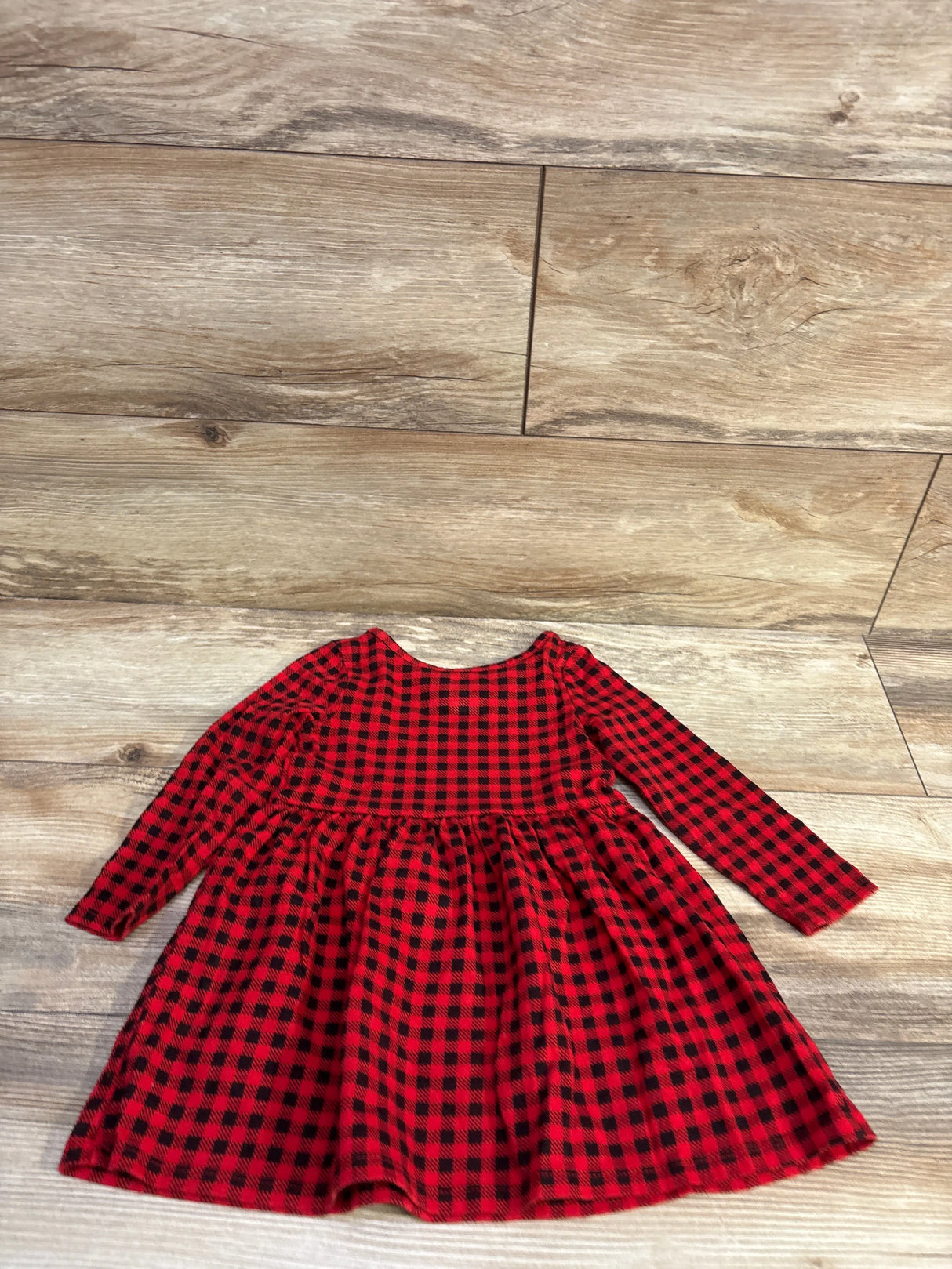 Flat lay of Cat & Jack toddler buffalo plaid dress showcasing long sleeves and gathered skirt on wood-look floor