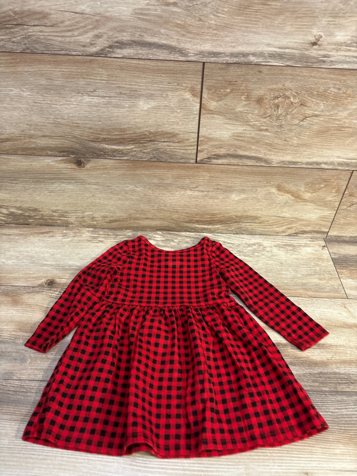Flat lay of Cat & Jack toddler buffalo plaid dress showcasing long sleeves and gathered skirt on wood-look floor