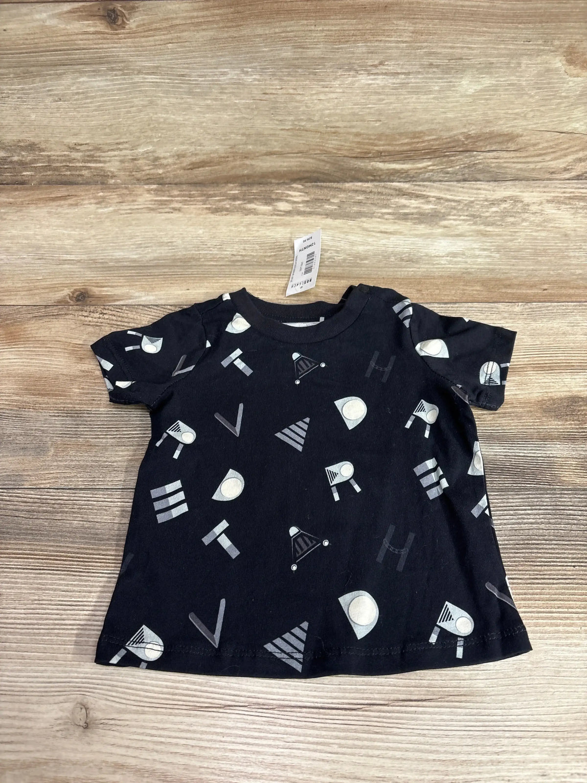 Flat lay of black Boxlunch x Star Wars baby T-shirt with allover print spelling Darth Vader on wood plank background