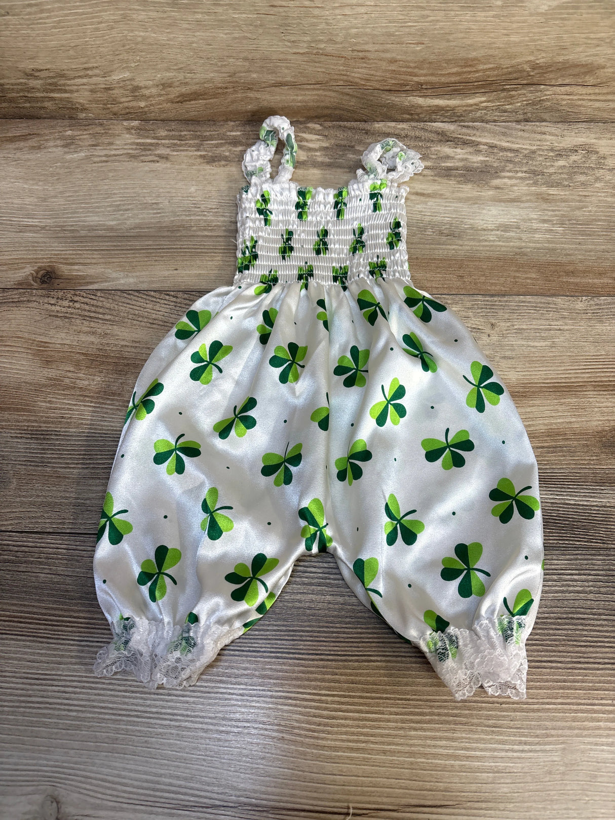 White baby romper with green shamrock print and lace trim on wooden background