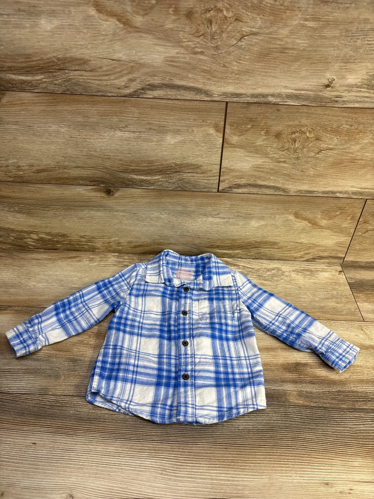 Blue and white plaid flannel long sleeve shirt for toddlers on a wood background