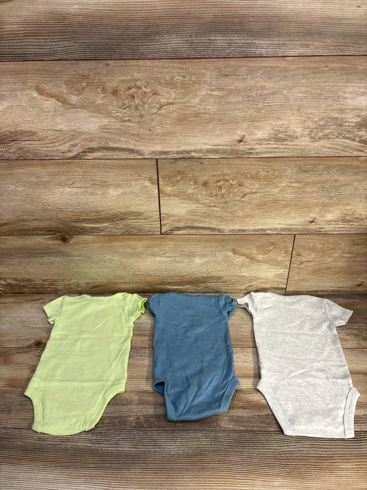 Front view of Carter’s 3pk Bodysuit Set Grey sz 3m showing three short-sleeve bodysuits on a wood surface