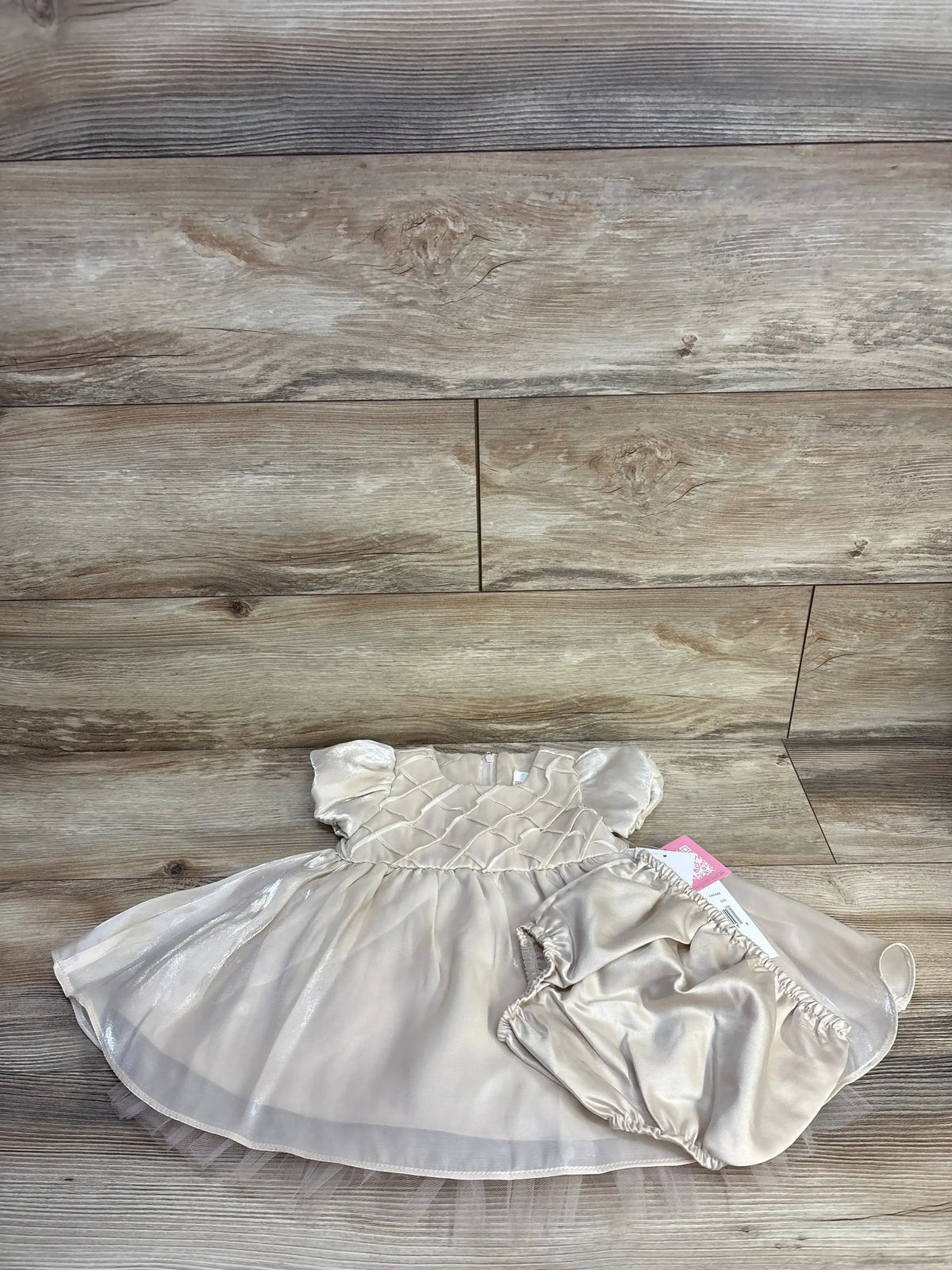 Flat-lay of gold baby dress and matching bloomers showing smocked bodice, puff sleeves and tulle skirt on wood background