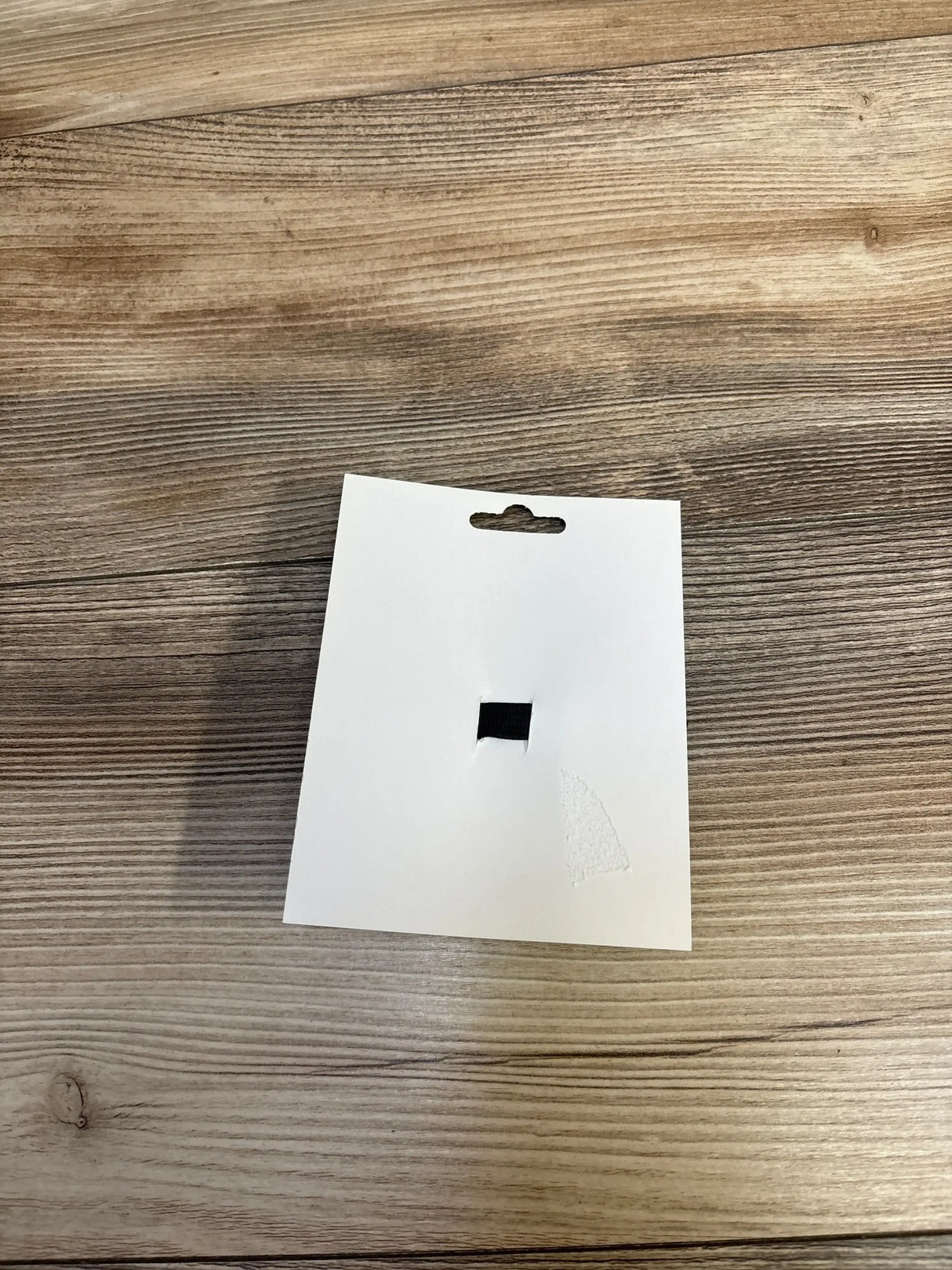 Blank white product tag with hang hole on wood surface, for kids or maternity items