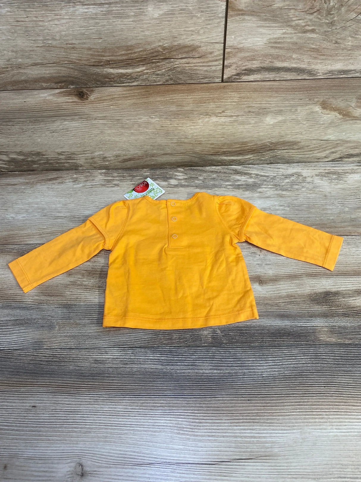 Flat lay of orange Boboli long-sleeve baby shirt, 3-6 months, back view showing three-button neck placket and puffed shoulders on wood floor