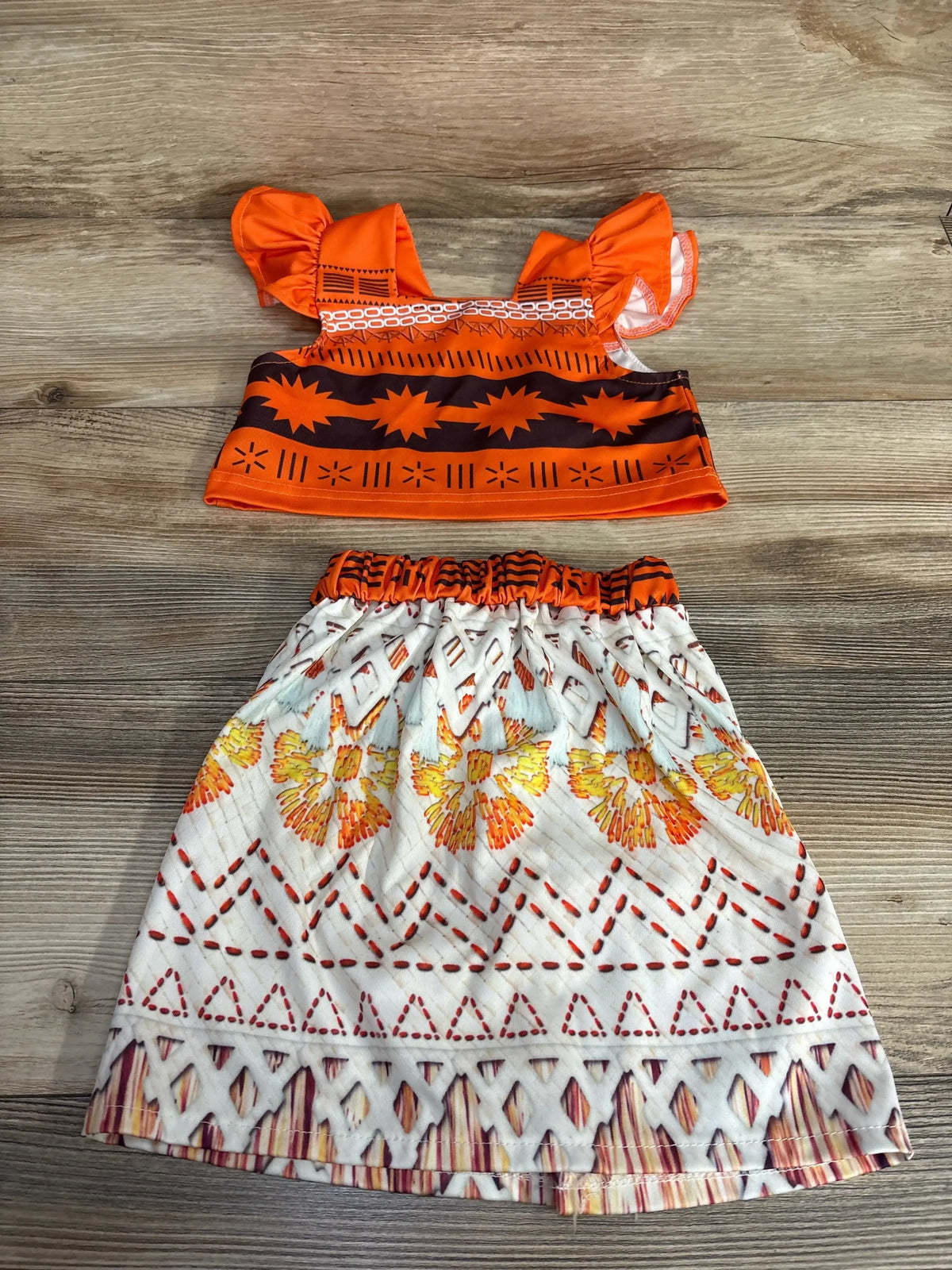 Two-piece toddler outfit with orange tribal-patterned top and white skirt with floral and geometric designs