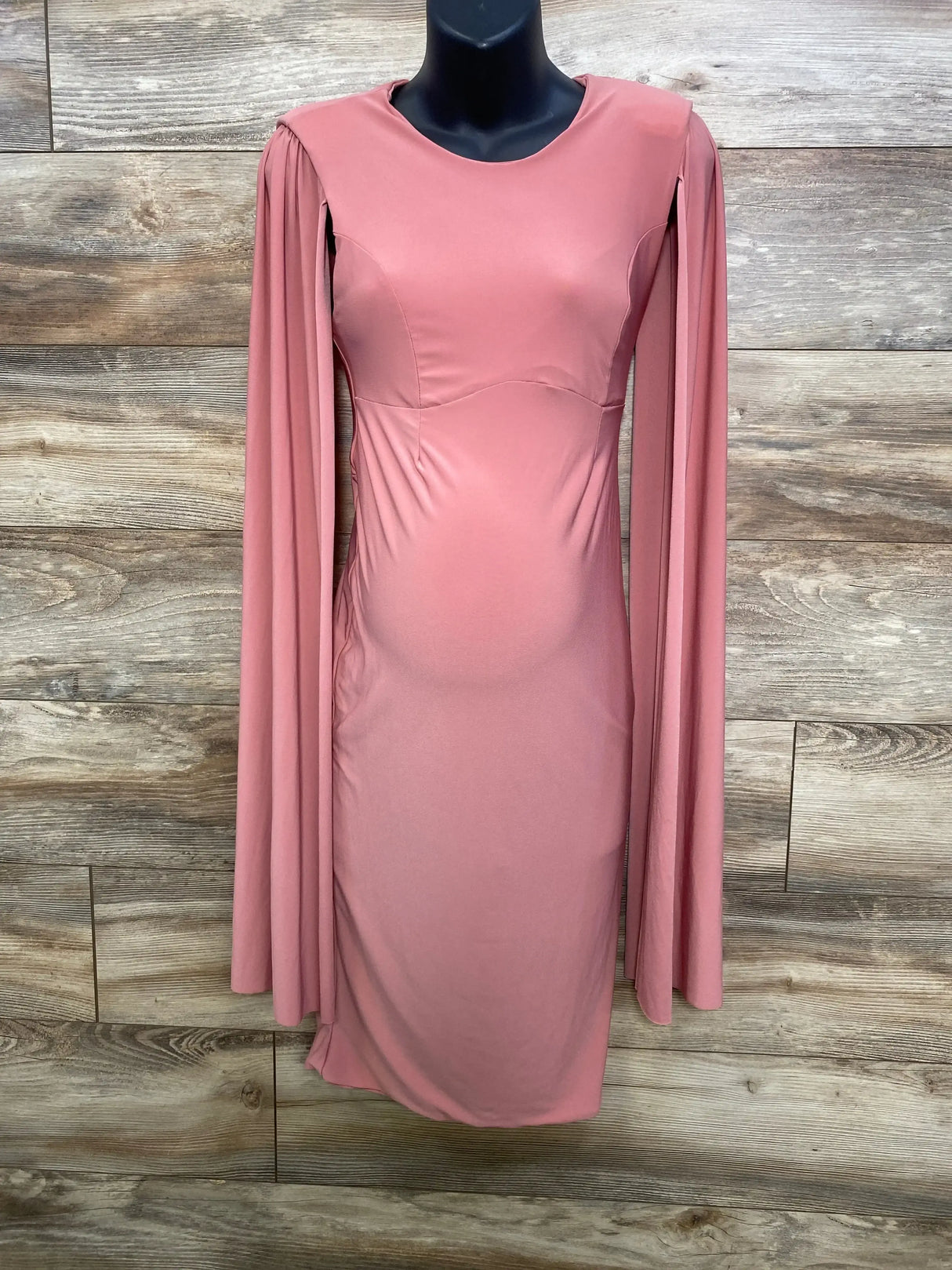Front view of Club L London maternity dress in pink on mannequin with cape sleeves and fitted silhouette on wood background