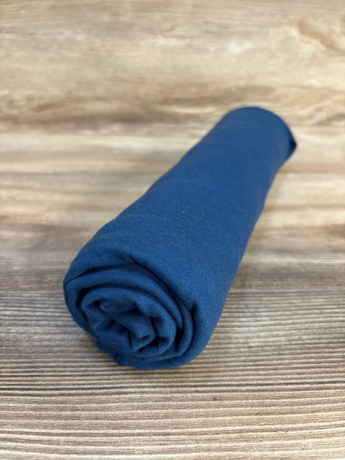 Angled view of Copper Pearl Robin knit swaddle blanket rolled to show knit texture and deep robin blue color on wooden surface