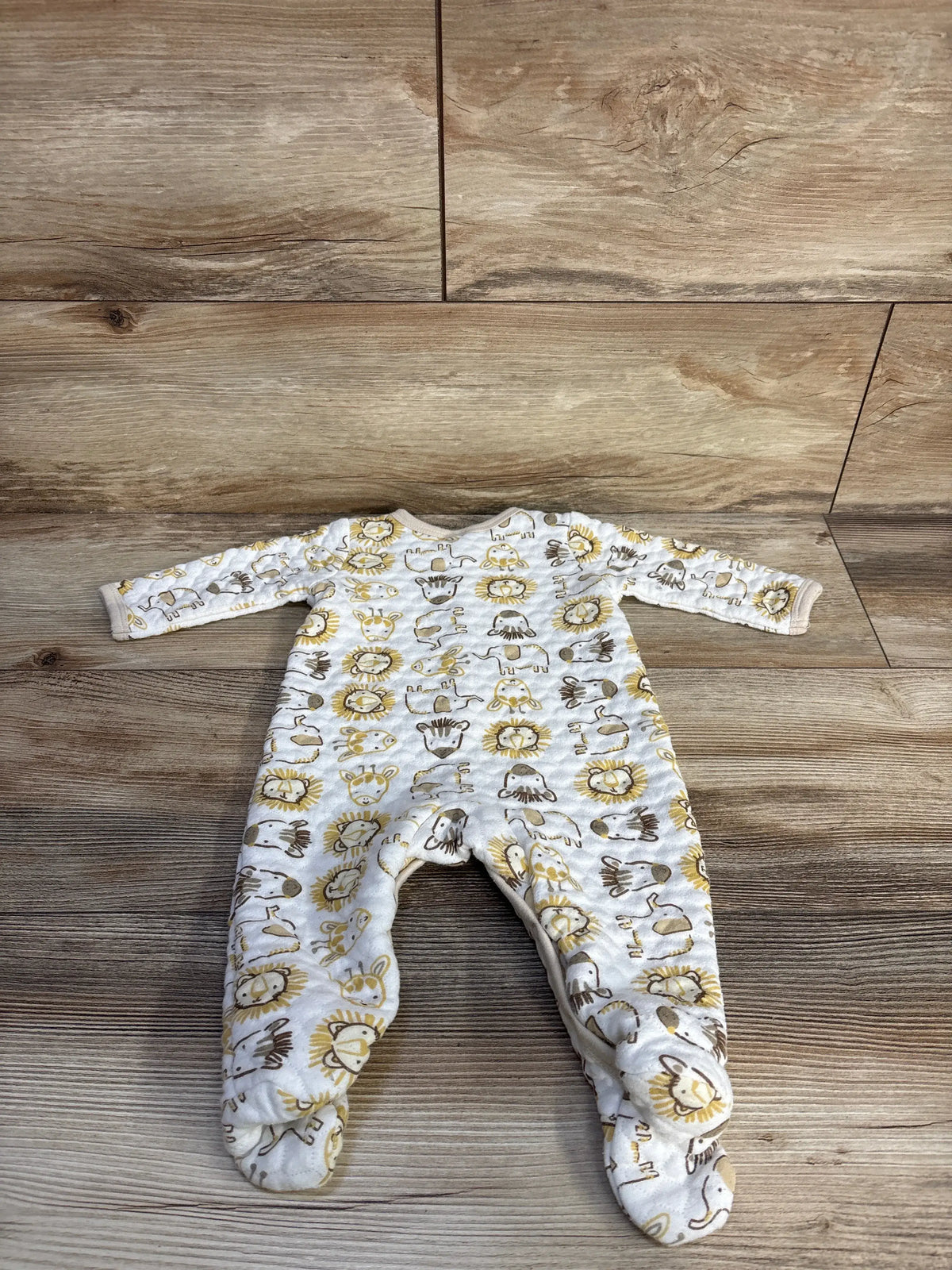 Top view of Little Beginnings white quilted sleeper showcasing animal print and footie design on wood background