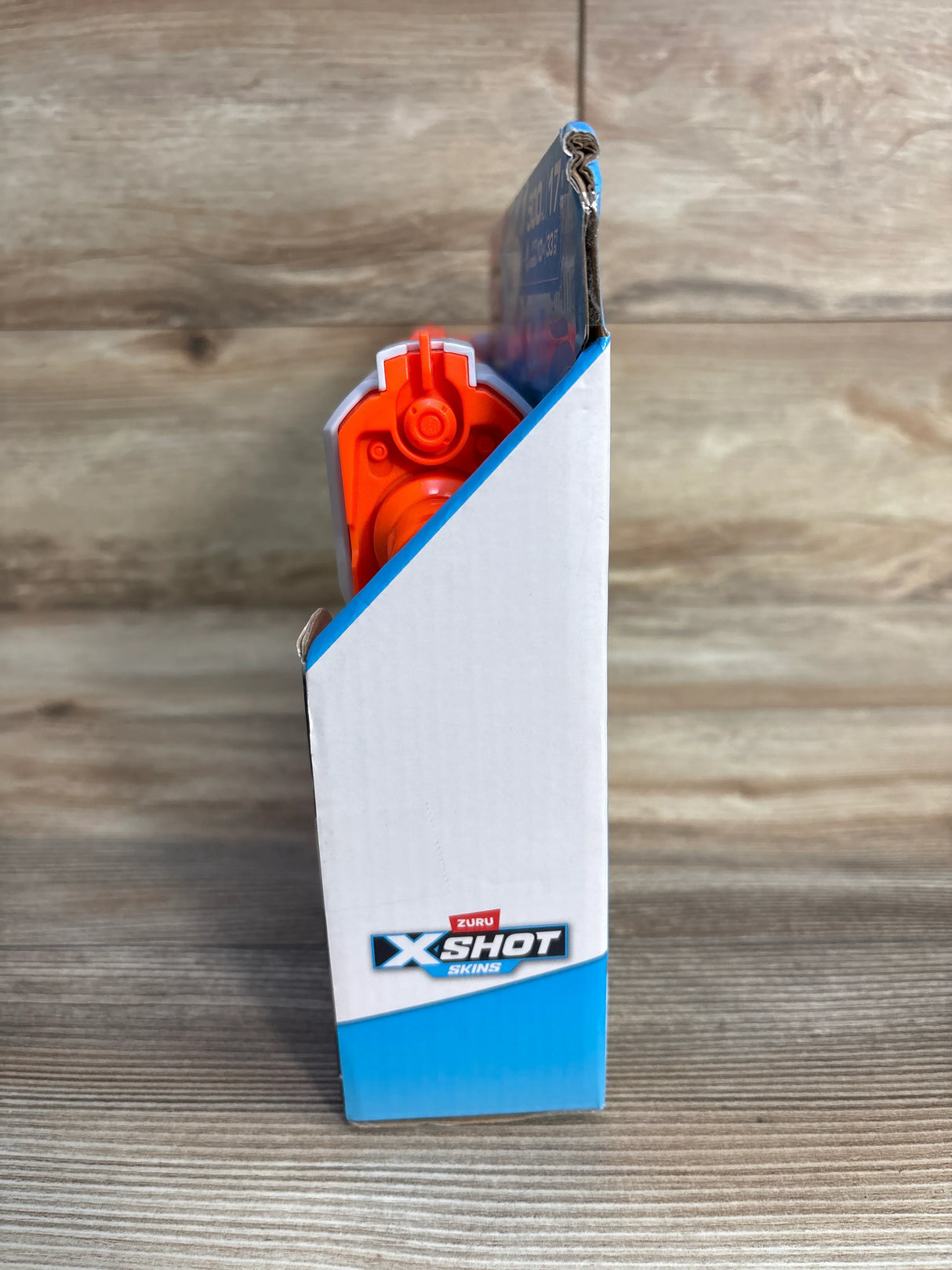 Zuru X-Shot Skins toy blaster partially visible in its packaging on a wood surface