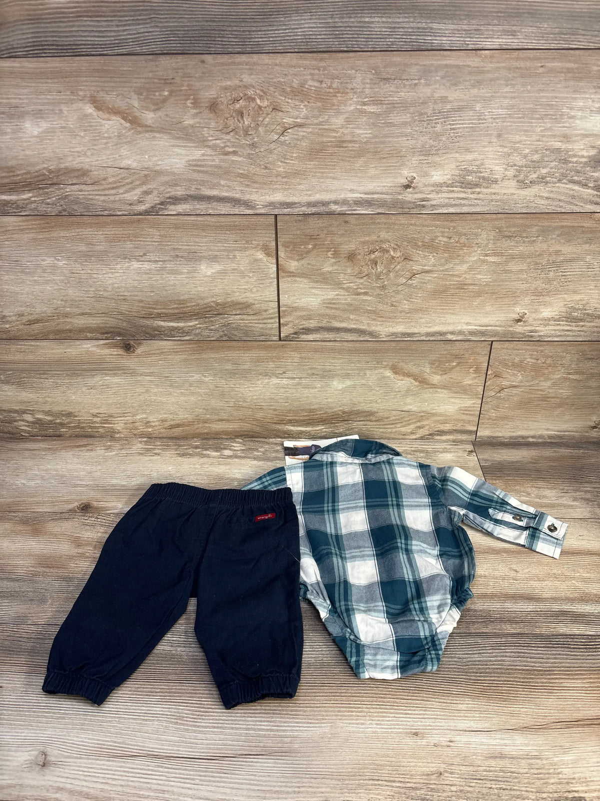 Top view of Wrangler bubble romper and pants set showcasing blue plaid romper with navy pants on wood background