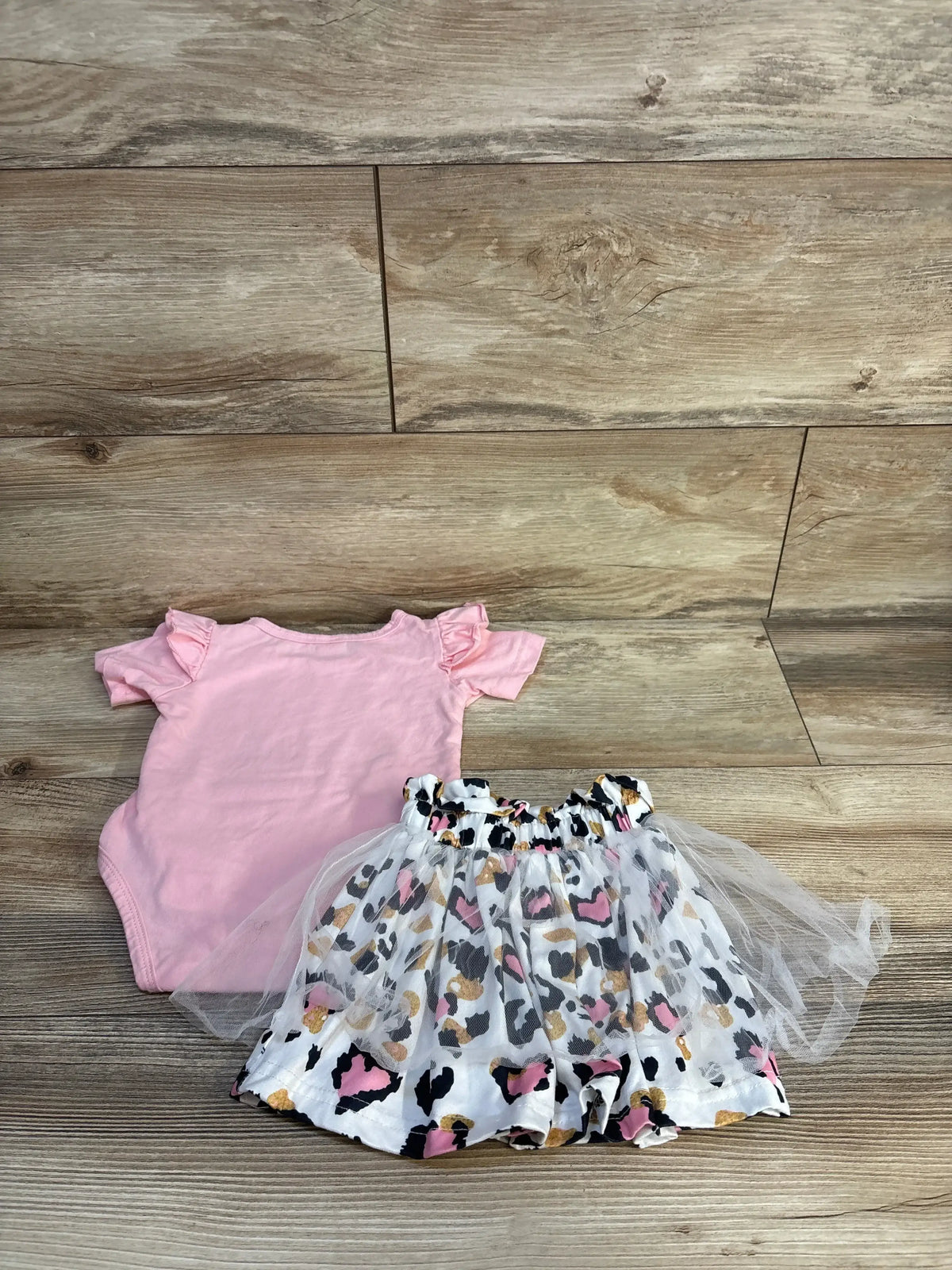 Flat lay of pink Babe bodysuit with ruffle sleeves and leopard print tulle skirt with elastic waist on wood backdrop