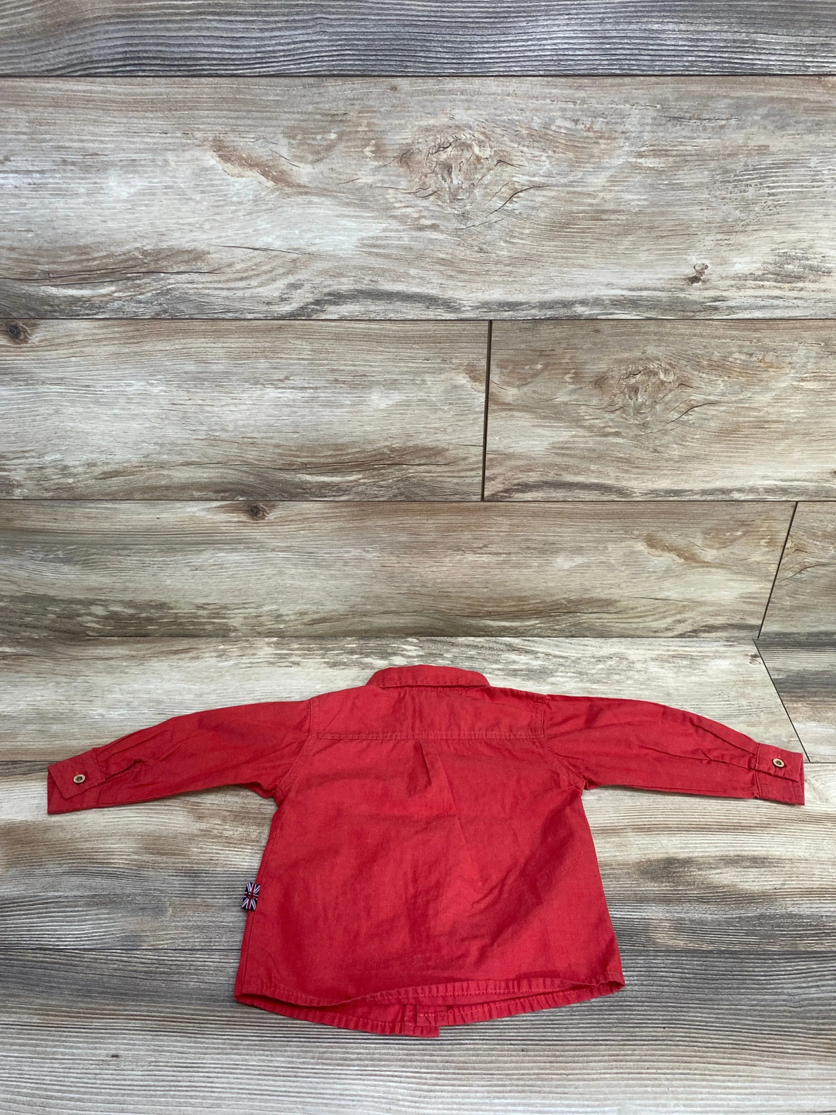 Back view of English Laundry toddler red button-up shirt showcasing long sleeves, button cuffs, and center back pleat on wood background