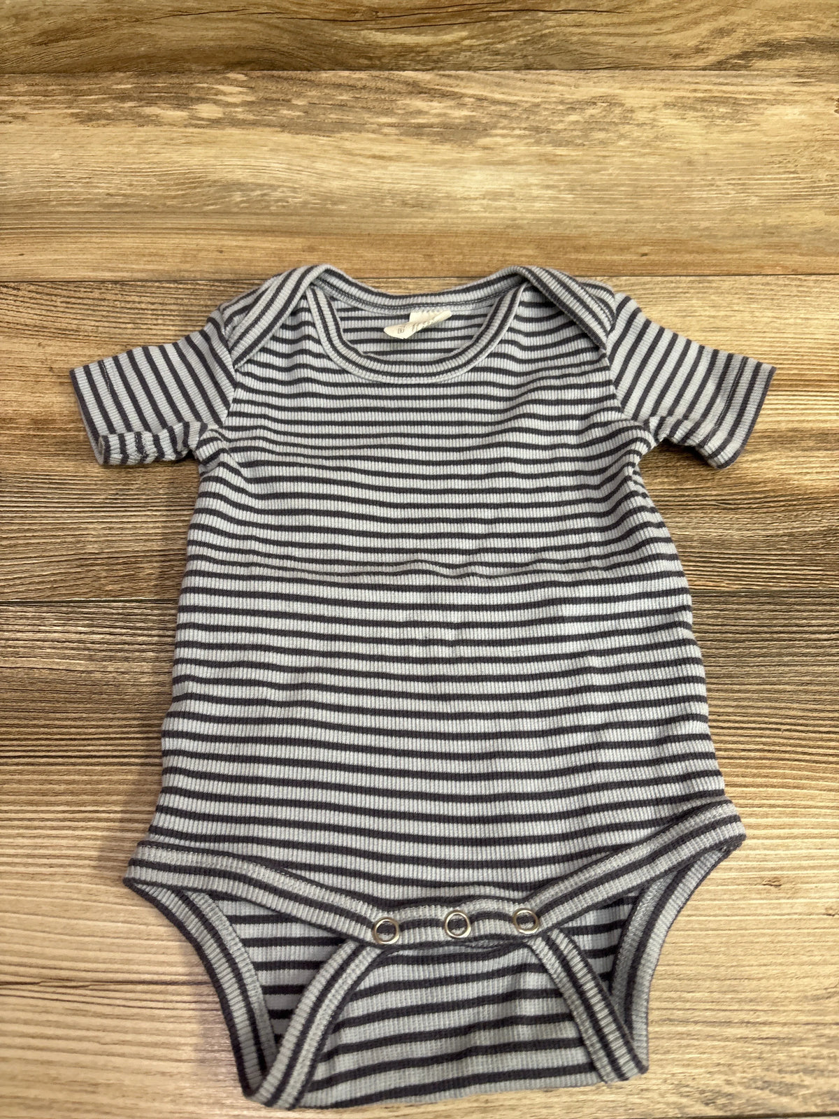Front view of Kate Quinn ribbed bodysuit in blue, size 3 to 6 months, with short sleeves and horizontal stripes on a wood background