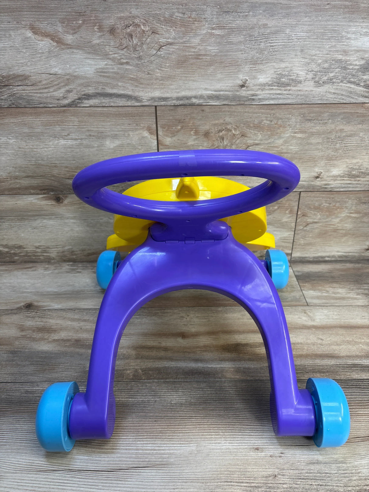Purple and yellow baby walker with blue wheels on wooden floor