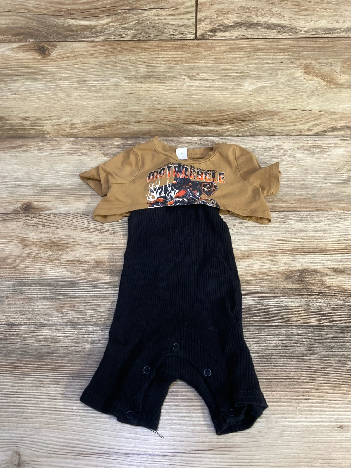 Flat lay of two-piece baby set brown cropped motorcycle tee and black ribbed romper with snap crotch on wood background