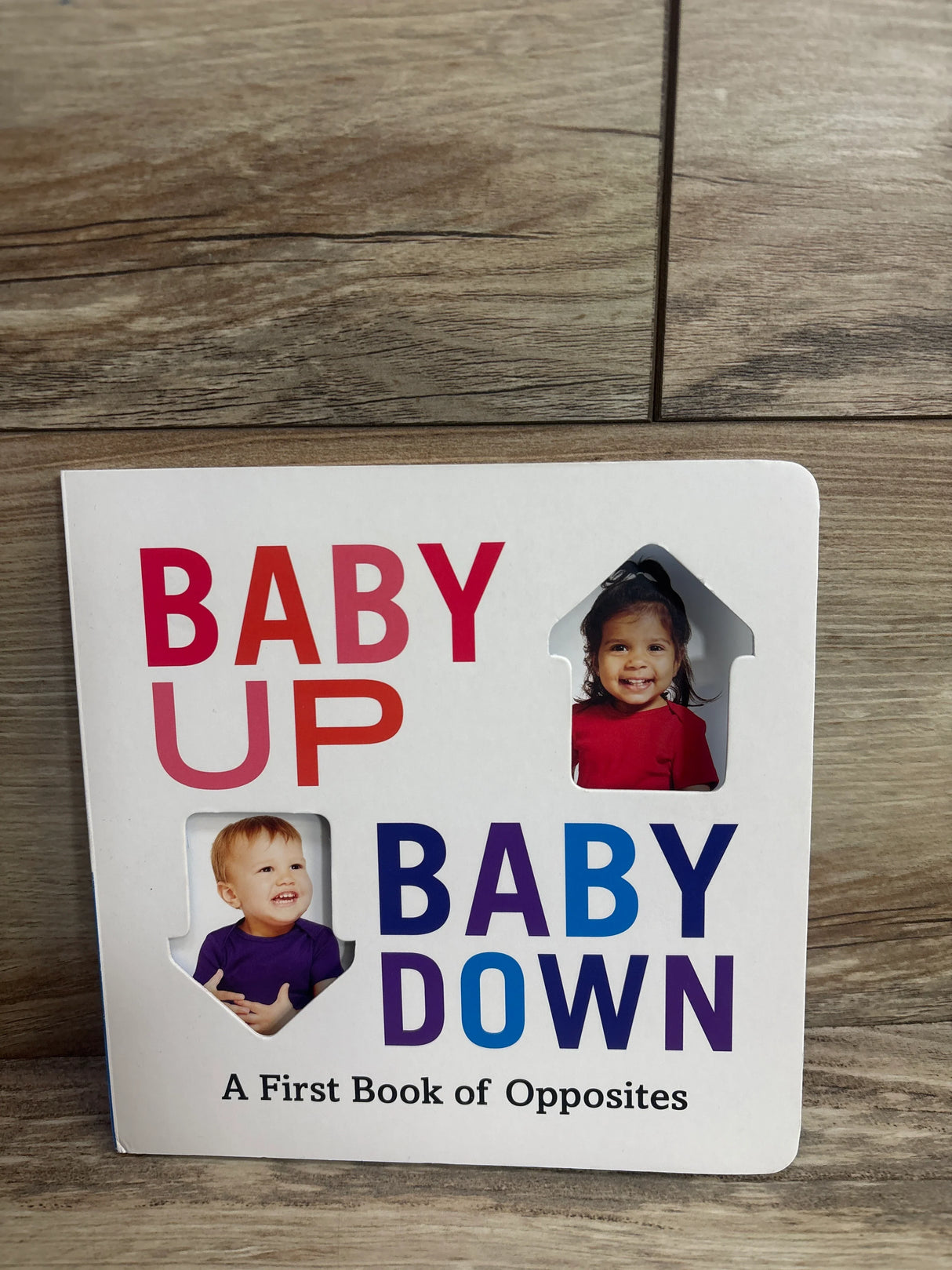 Children's board book titled Baby Up Baby Down with smiling baby photos and colorful text on wooden background
