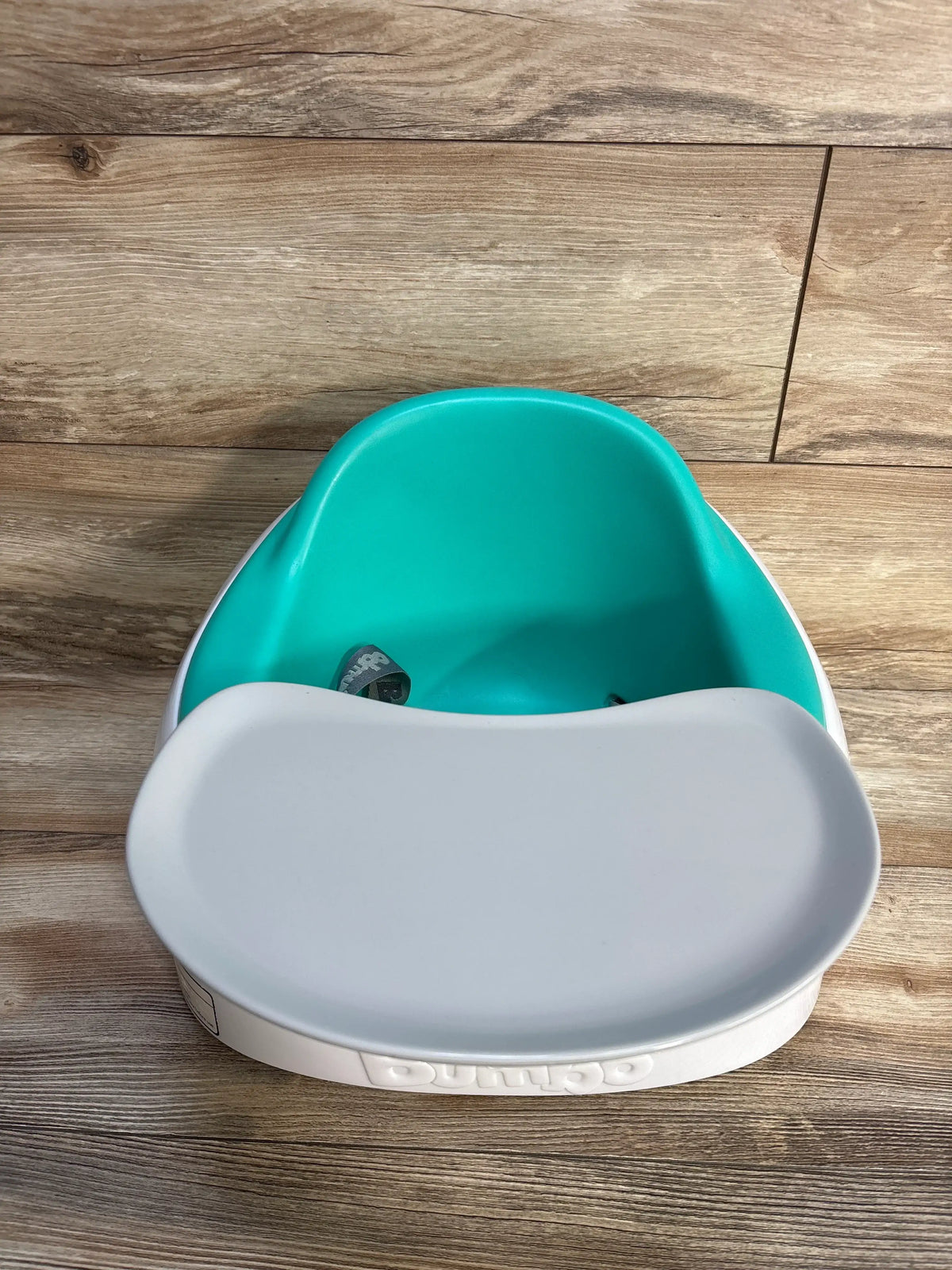 Front view of Bumbo Multi Seat showcasing removable tray and teal seat with a wood-look floor background