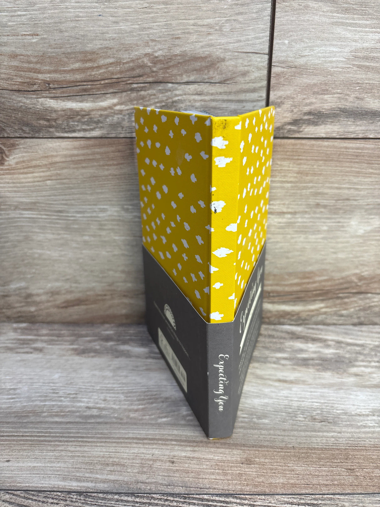 Yellow and gray hardcover book with white spots, titled 'Expecting You,' on wood surface