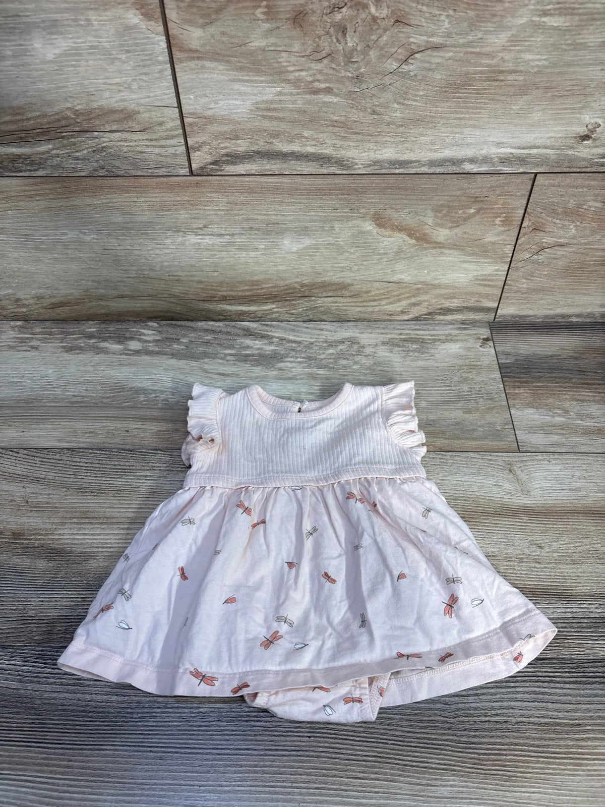 Front view of Carter’s pink bodysuit dress with ribbed bodice, ruffled sleeves, and printed skirt on wood floor