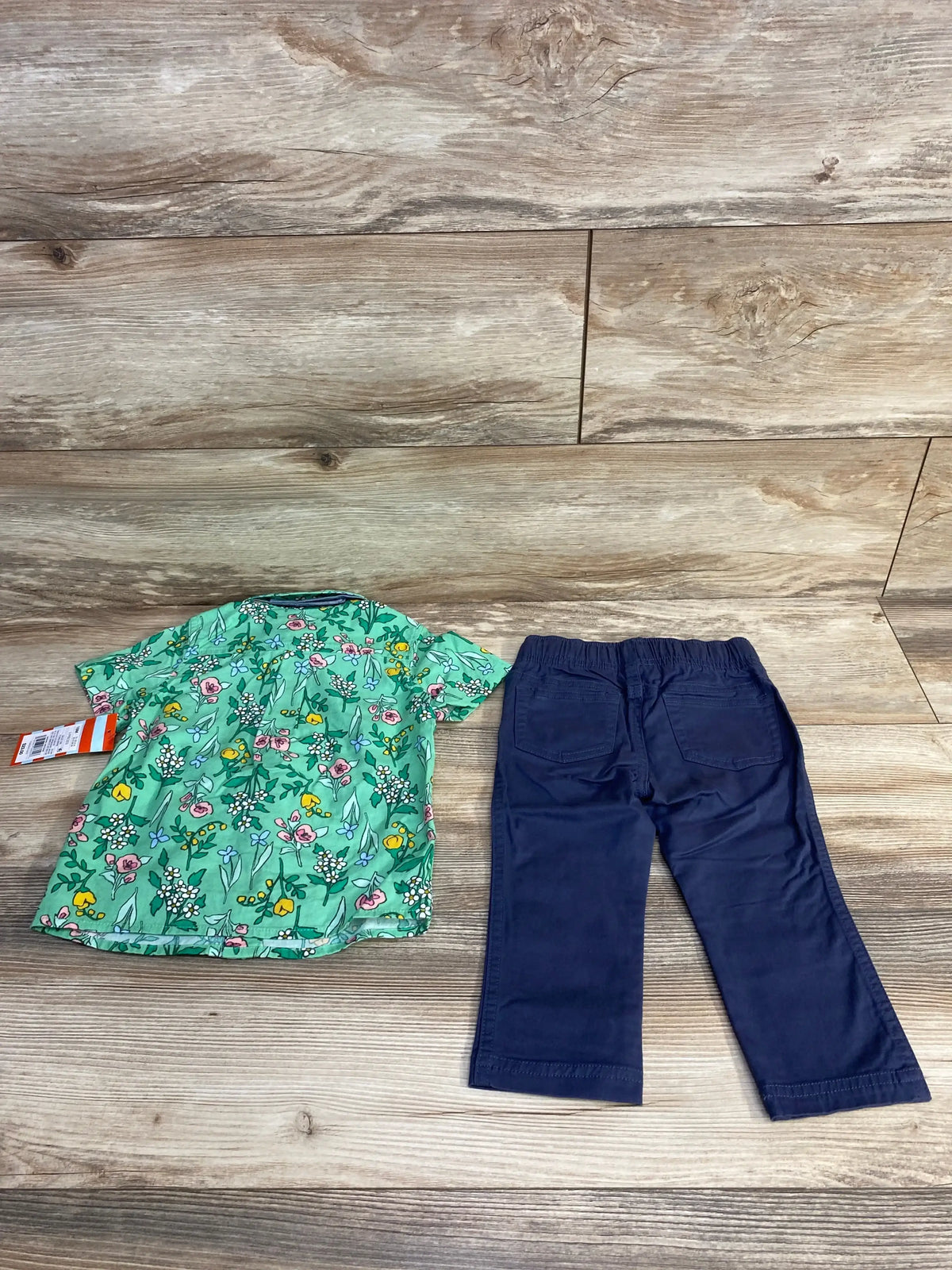 Flat lay of toddler green floral button-up shirt and navy pants showing all-over floral print and elastic waist on wood plank background