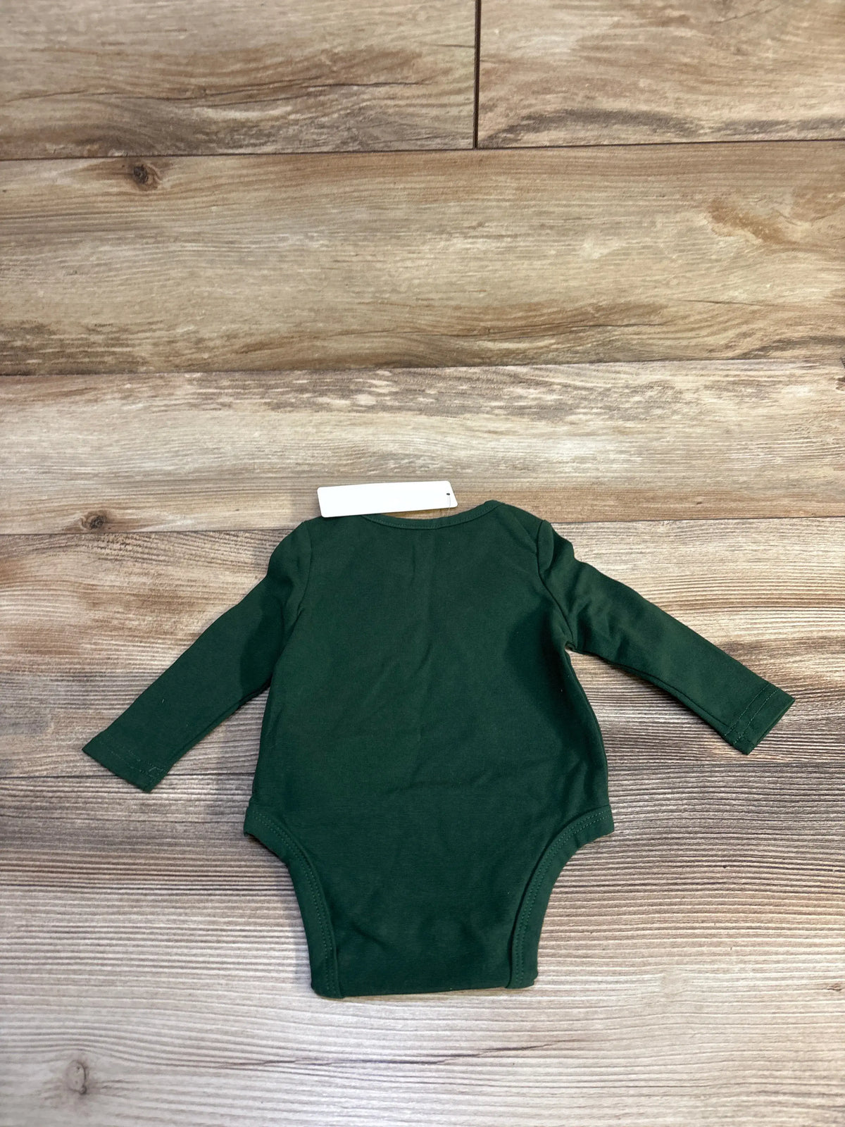 New Cozy Cub long sleeve baby bodysuit in dark green, size 0-1m, on a wood background.