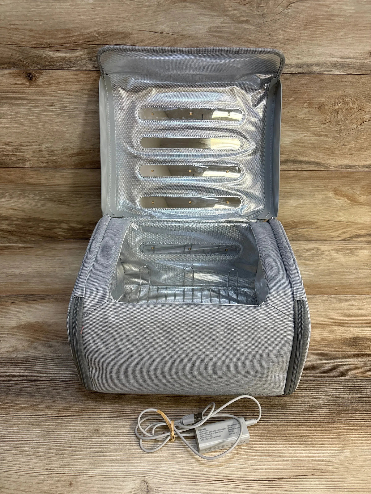 Open view of Munchkin 59S UV cleaning bag showing reflective interior, removable rack, and USB power adapter on wood background