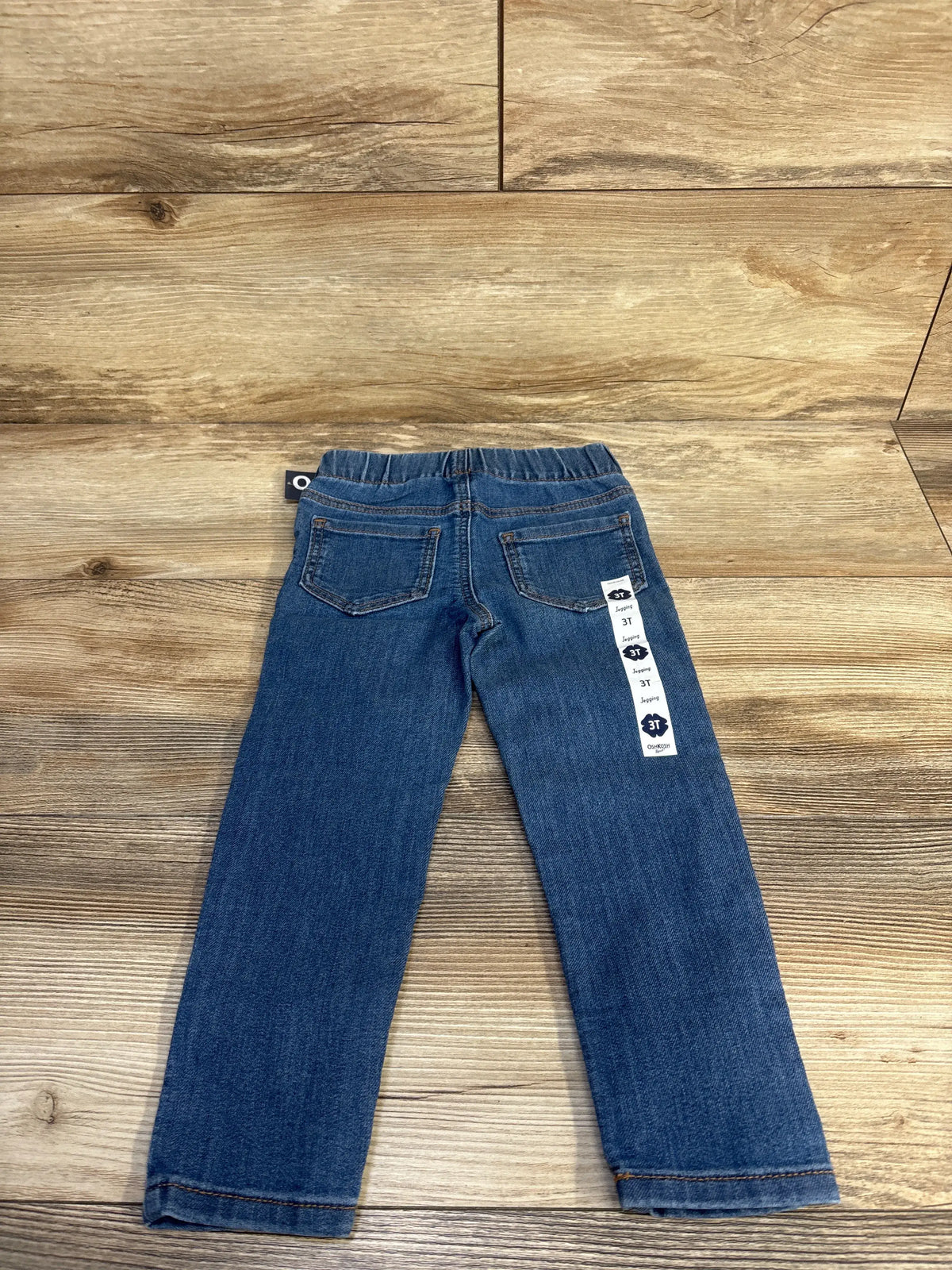 Back view of OshKosh medium wash pull-on jeggings in blue, size 3T, showing elastic waist, back pockets, and full-length legs