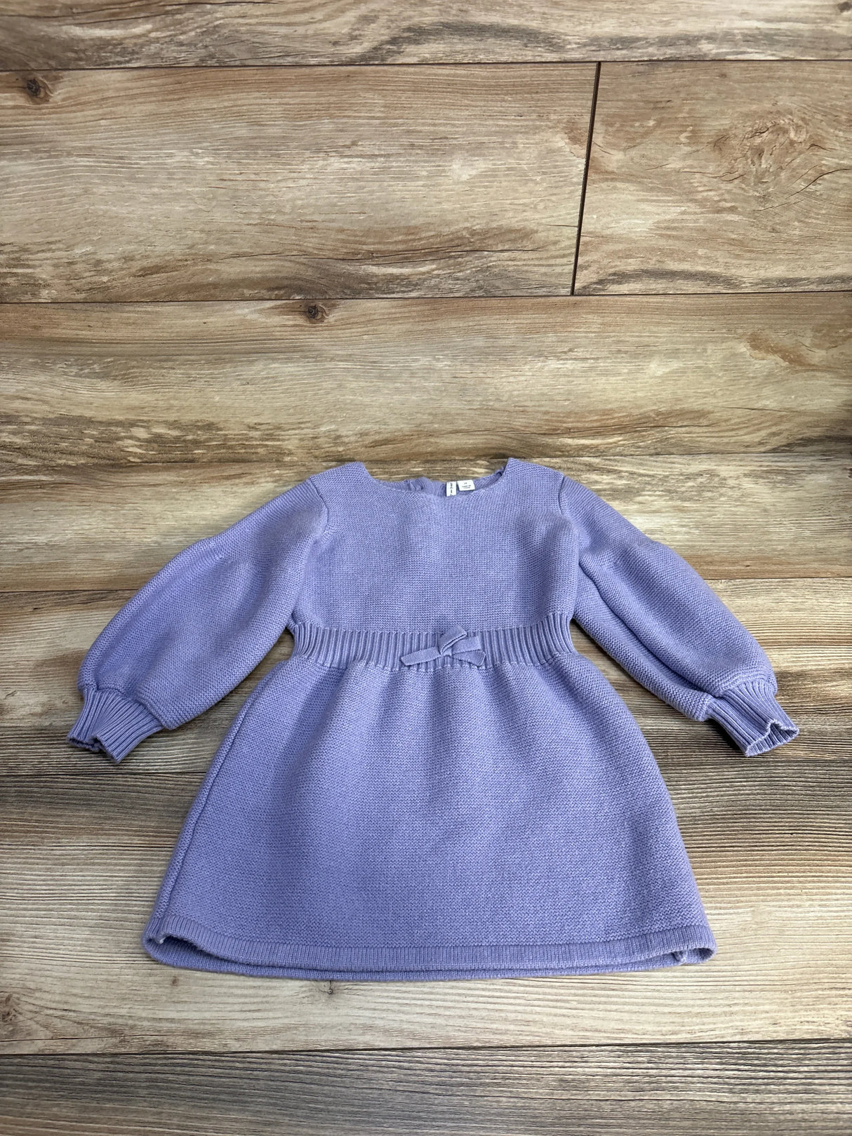 Lavender long-sleeve knitted baby dress with puff sleeves and a bow on wooden floor