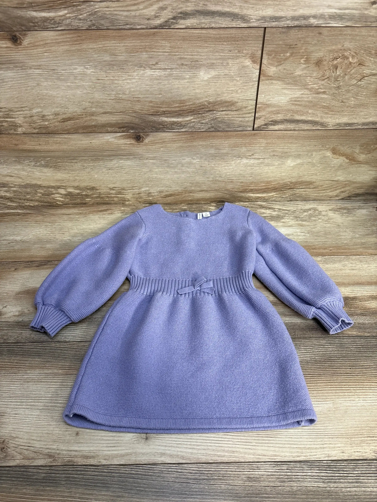 Lavender long-sleeve knitted baby dress with puff sleeves and a bow on wooden floor