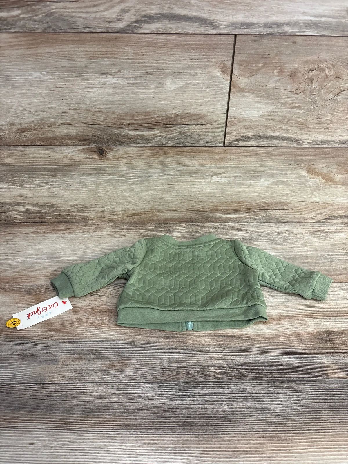 Green quilted baby jacket with geometric pattern laid flat on wooden floor