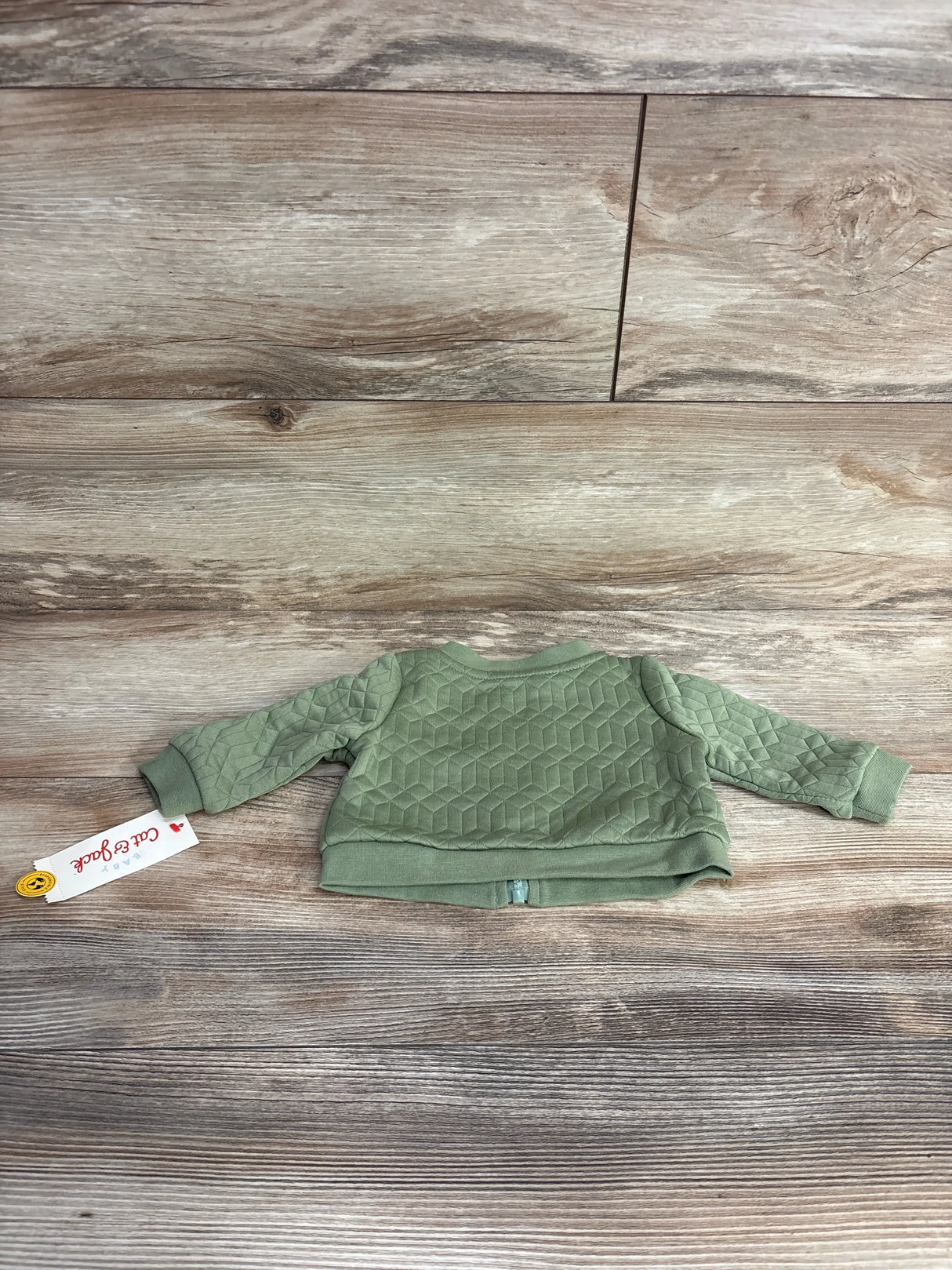 Green quilted baby jacket with geometric pattern laid flat on wooden floor