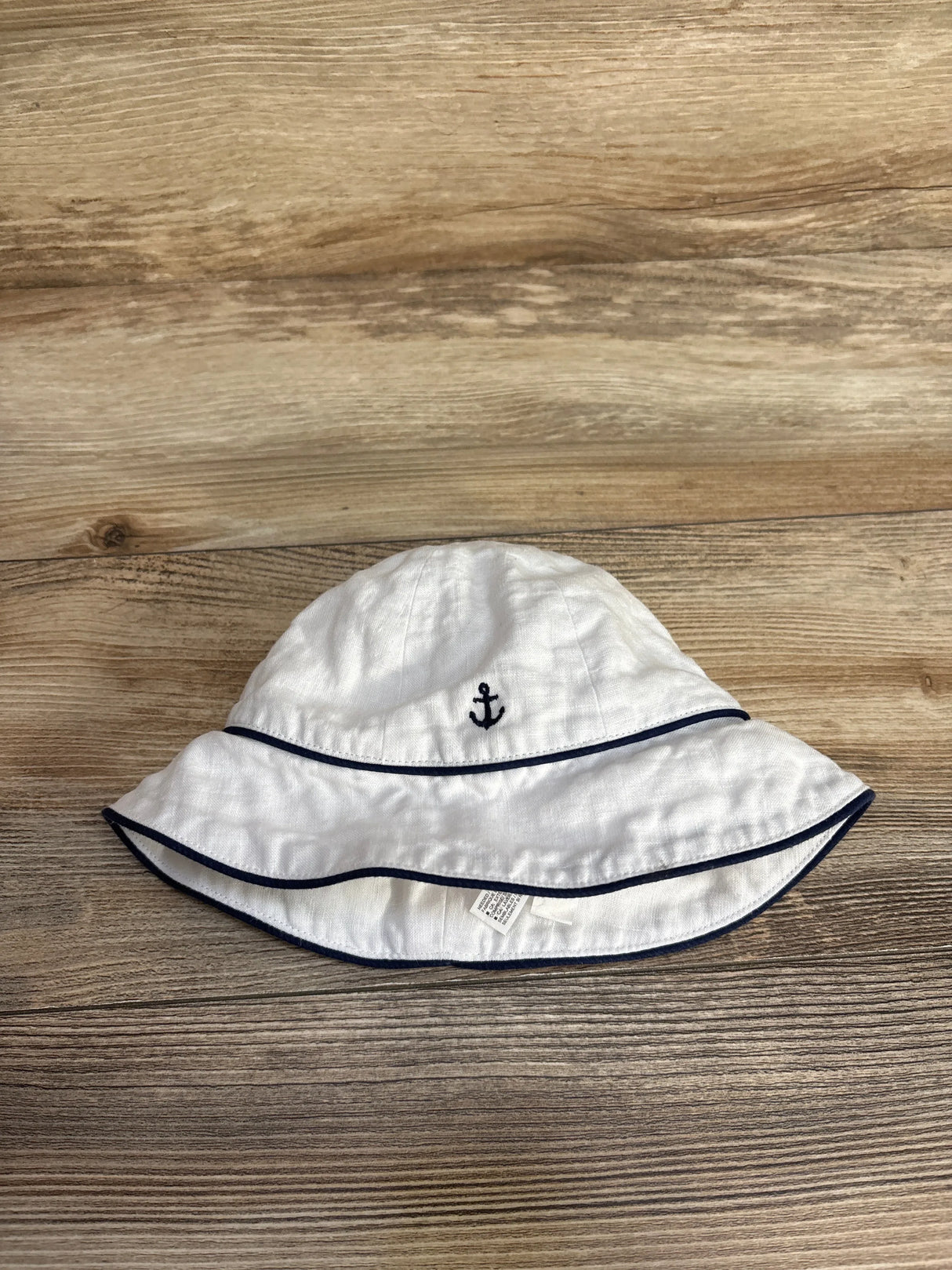 White baby bucket hat with navy blue anchor embroidery and trim on wooden surface