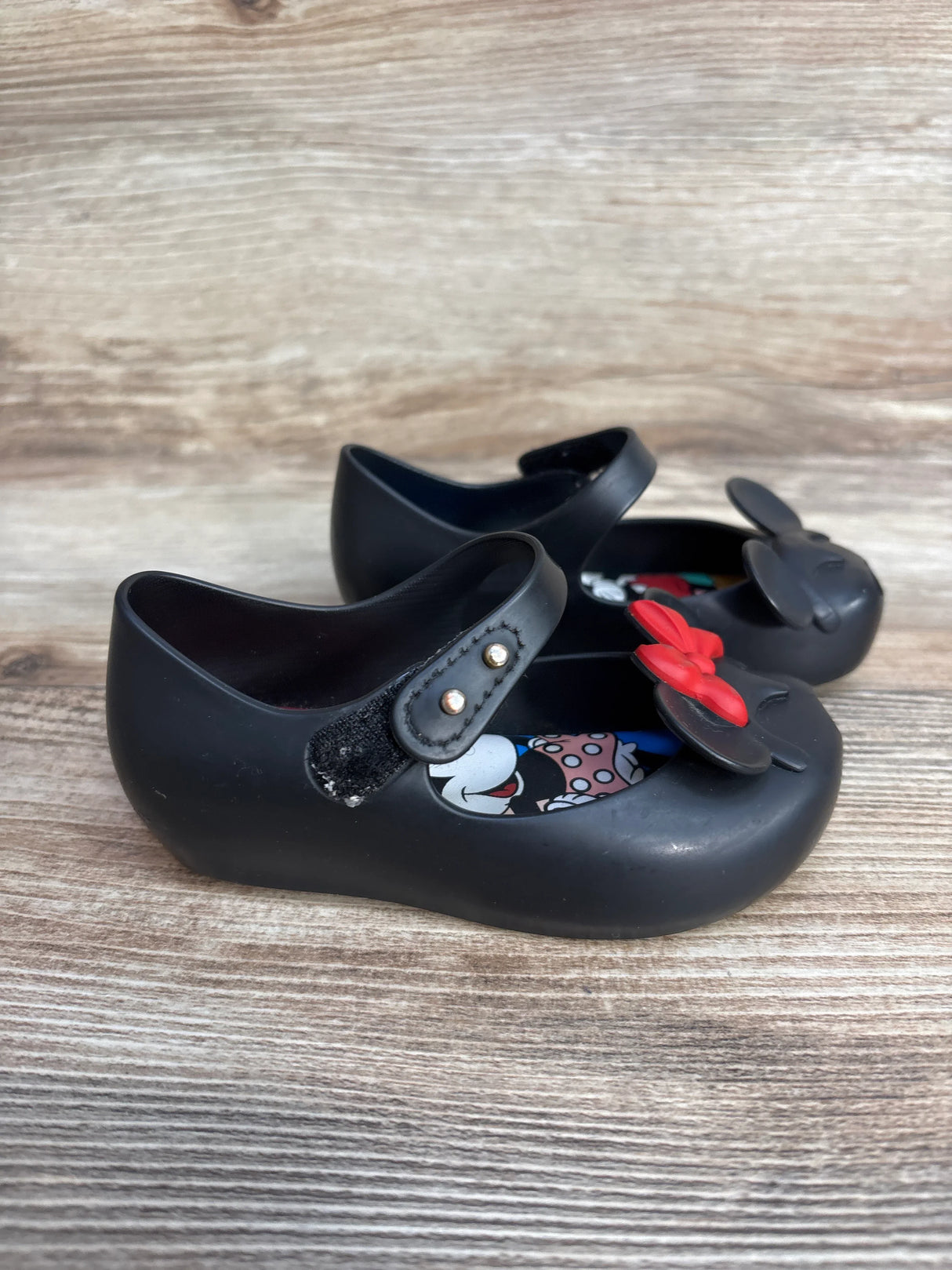 Black children's Mary Jane shoes with red bows and Minnie Mouse insole on wooden surface