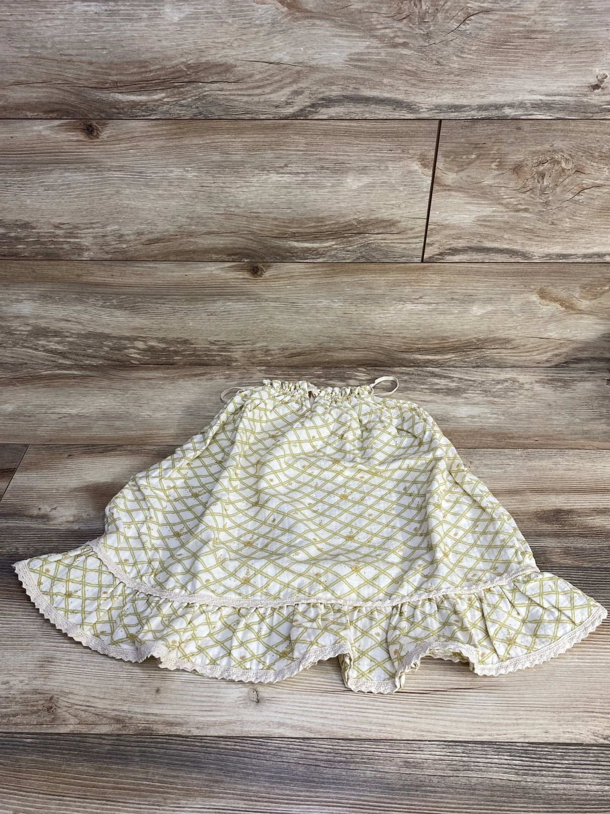 Flat lay of Liilu organic sleeveless toddler dress (ecru, 4T) with ruffled hem and yellow lattice print on wood background