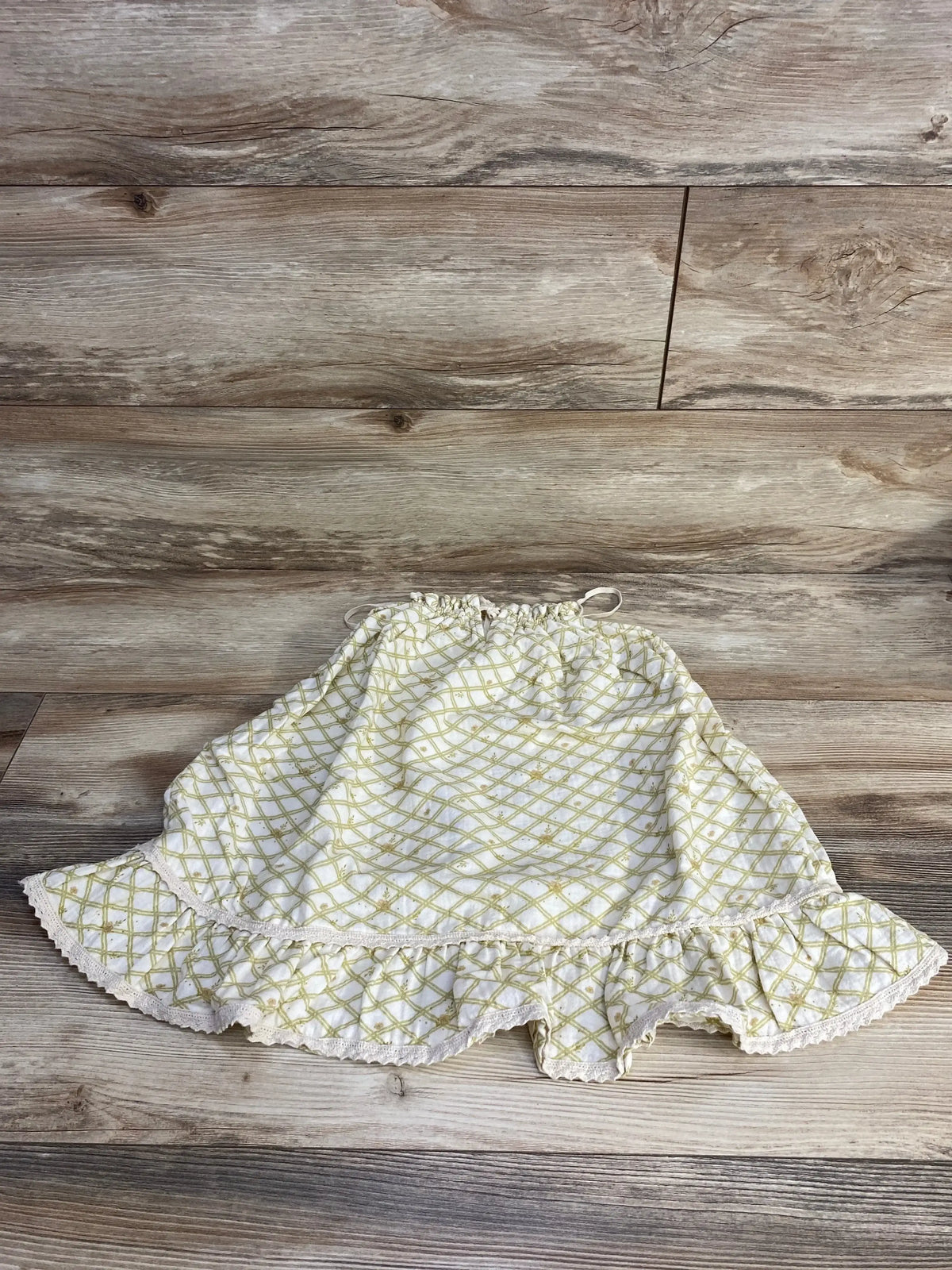 Flat lay of Liilu sleeveless toddler dress showcasing yellow lattice print and ruffled hem on wood background