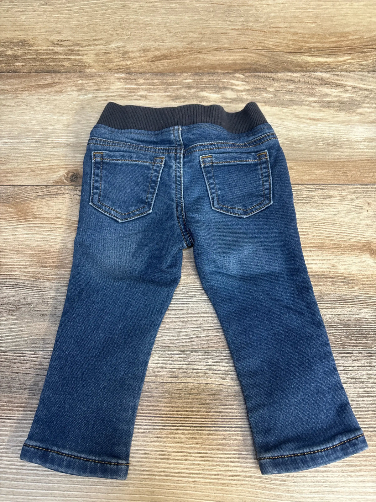 Back view of baby jeans with elastic waistband and back pockets laid flat on wood plank background