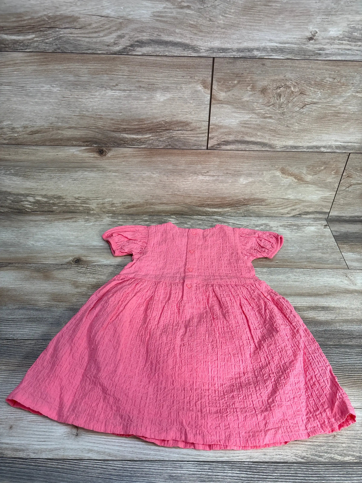 Pink textured cotton girl's dress with short sleeves on wood background