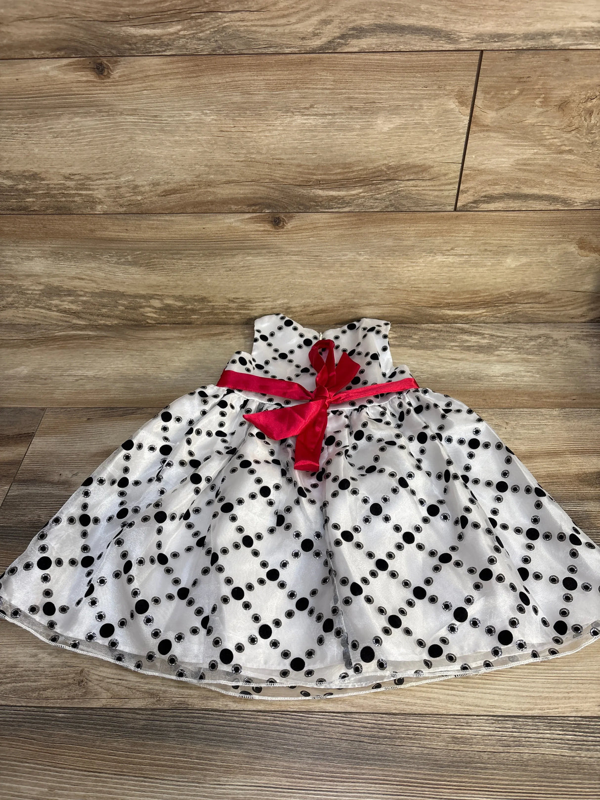 Flat lay of white Love by Special Occasions toddler polka dot dress showing black polka dots and red sash on wood floor
