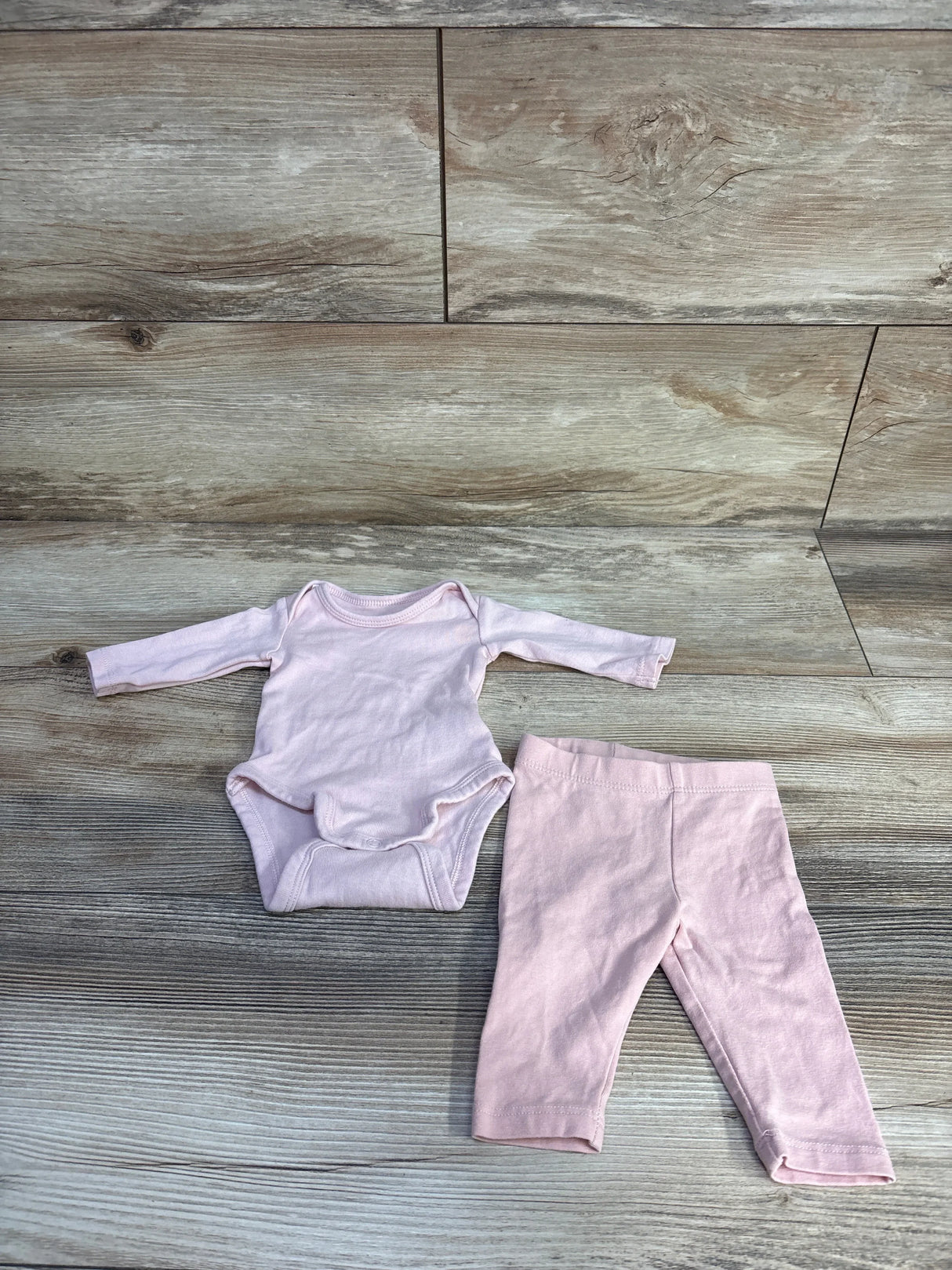 Flat lay of H&M preemie pink long-sleeve bodysuit and matching pants showing snaps and elastic waist on wood background