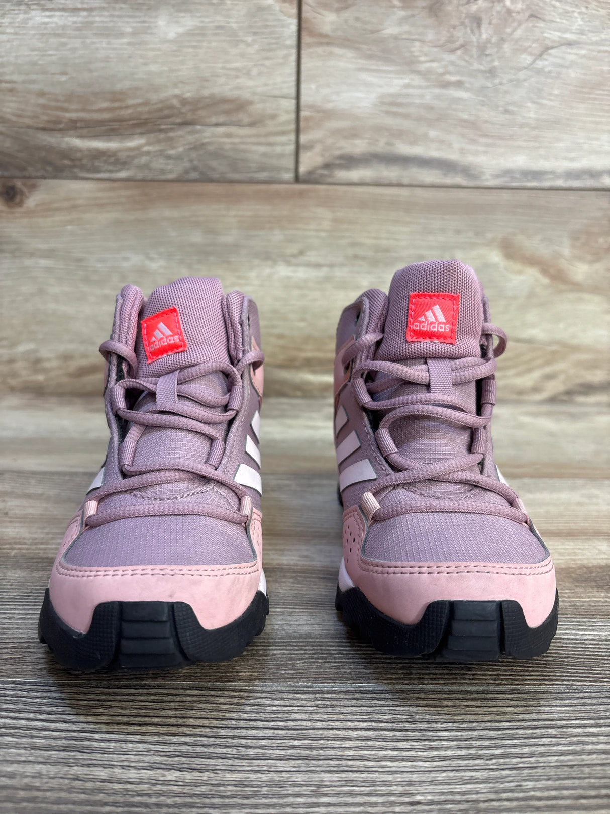Pink kids adidas sneakers with white stripes and black soles on wood background