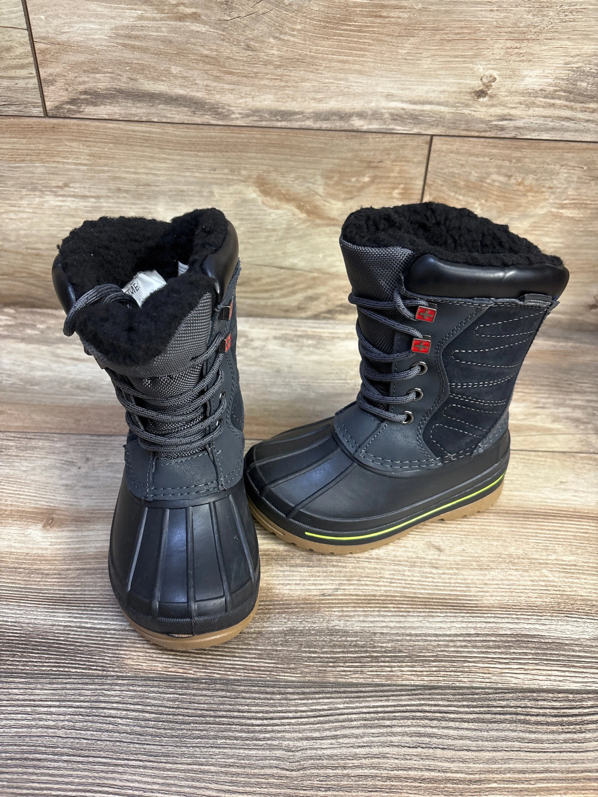 Three-quarter view of Swiss Tech kids’ black winter boots size 9C showcasing rubber lower, faux-fur lining and lace-up shaft with wood floor background