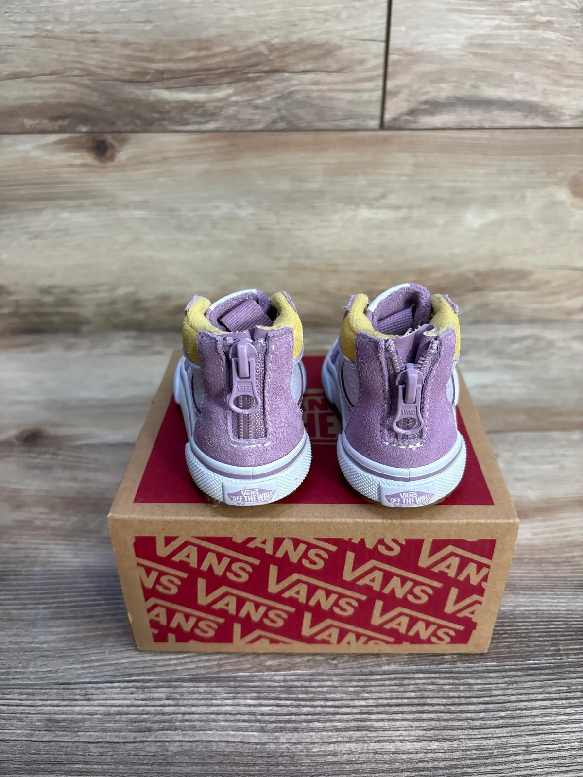 Rear view of purple Vans MTE Sk8 Hi-Zip toddler sneakers showcasing back zippers with a Vans shoebox on a wood floor