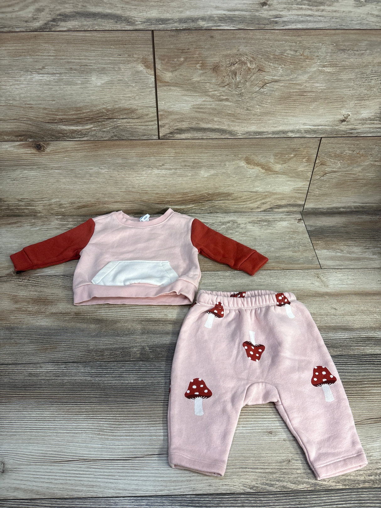 Pink baby outfit with red mushroom print pants and long sleeve top on wood background